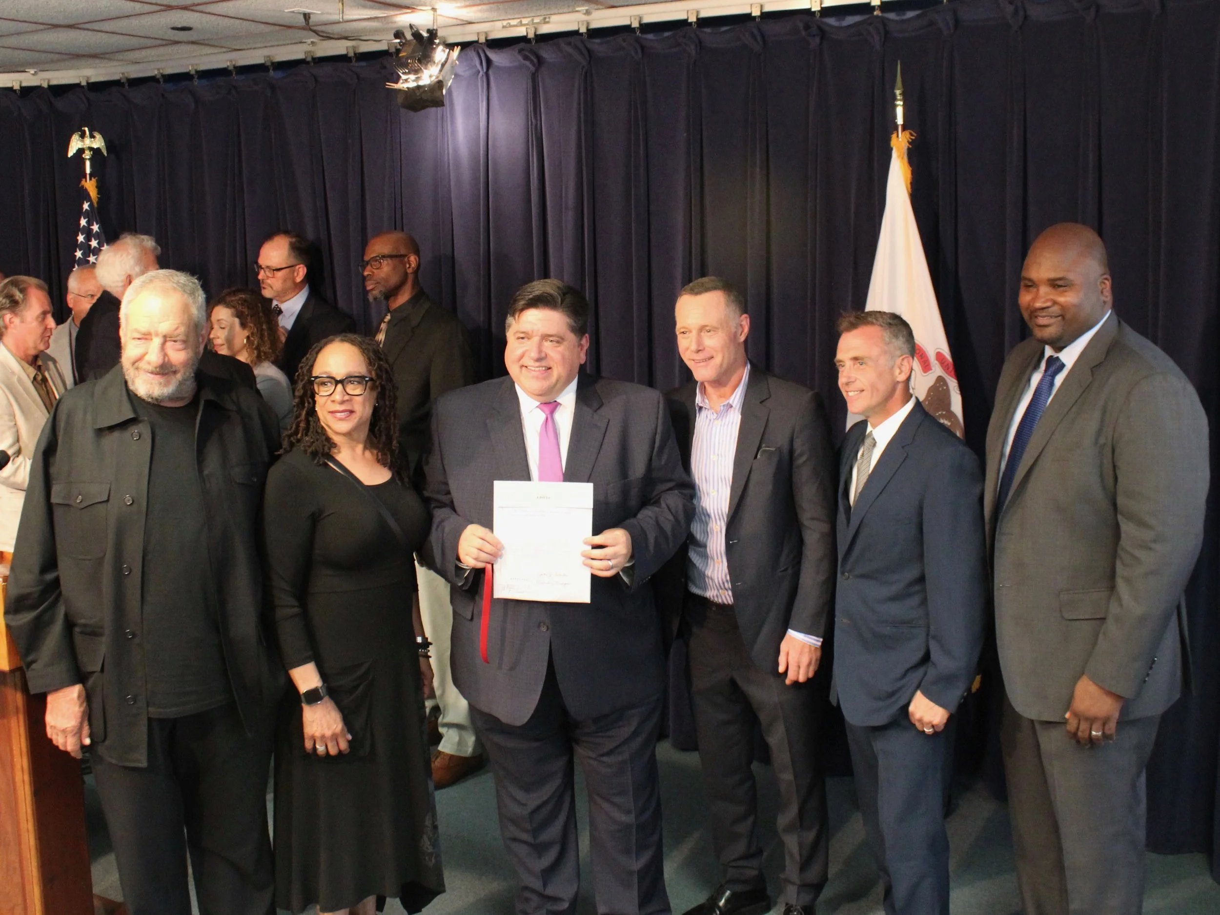 Gov. Pritzker brandishes extension of the film tax credit, joined by state Sen. Elgie Sims (right) along with TV producer Dick Wolf and actors S. Epatha Merkerson of “Chicago Med,” Jason Beghe of “Chicago P.D.,” and David Eigenberg of “Chicago Fire.”