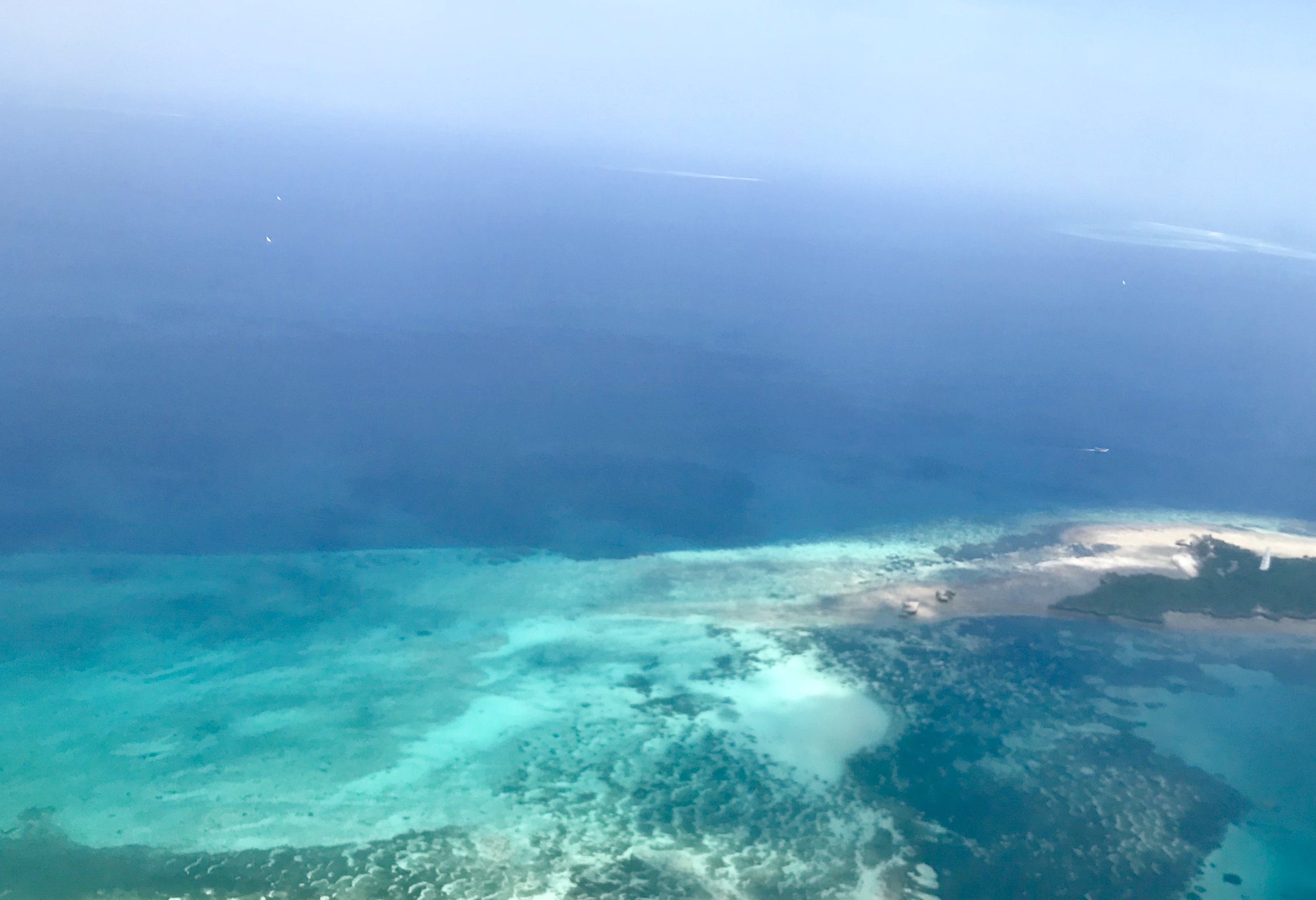Aerial view of a coastline with clear turquoise waters and a beach with some boats and trees.