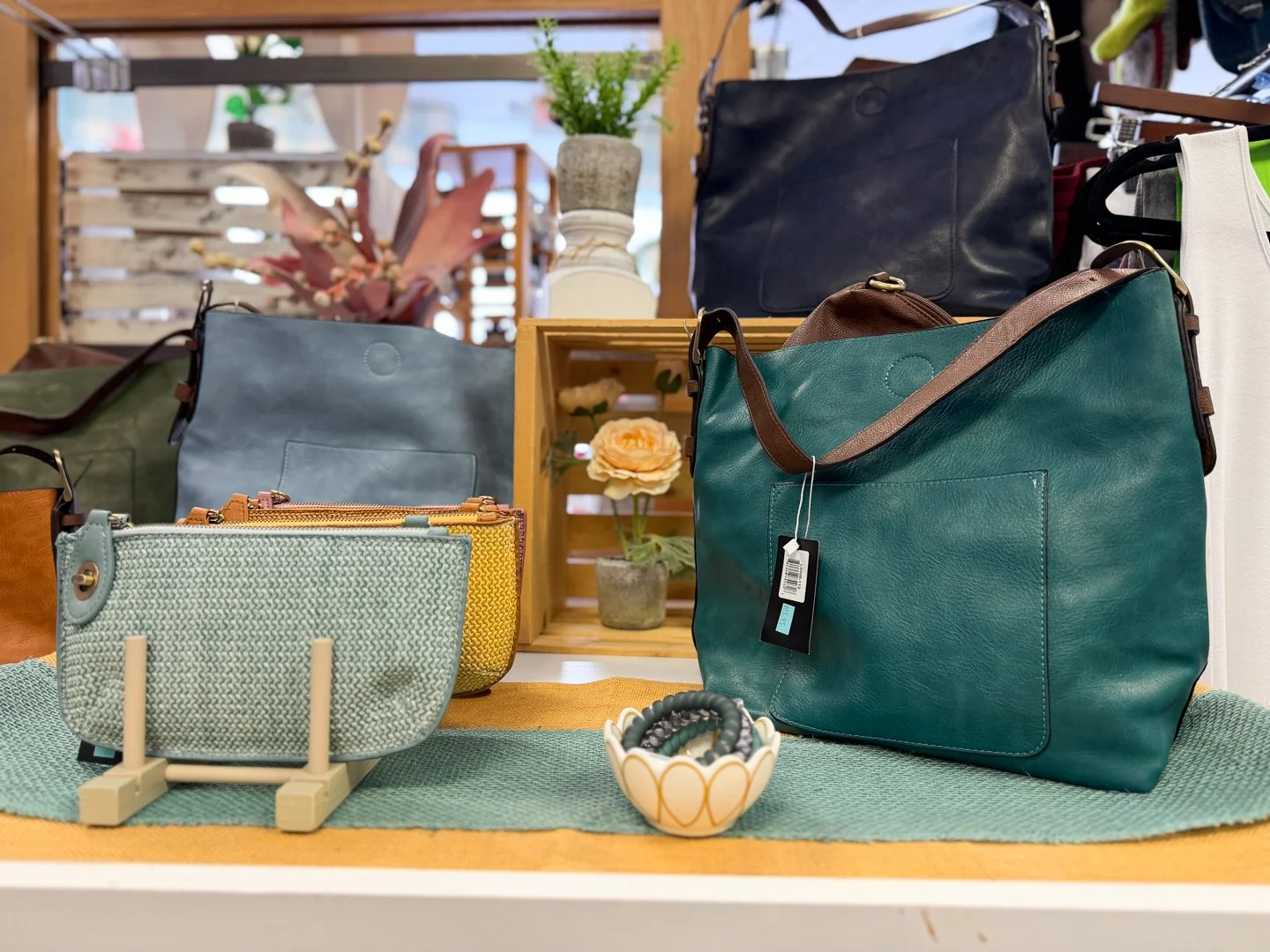 Display of teal and navy leather tote bags alongside a small mint green woven clutch on a retail shelf