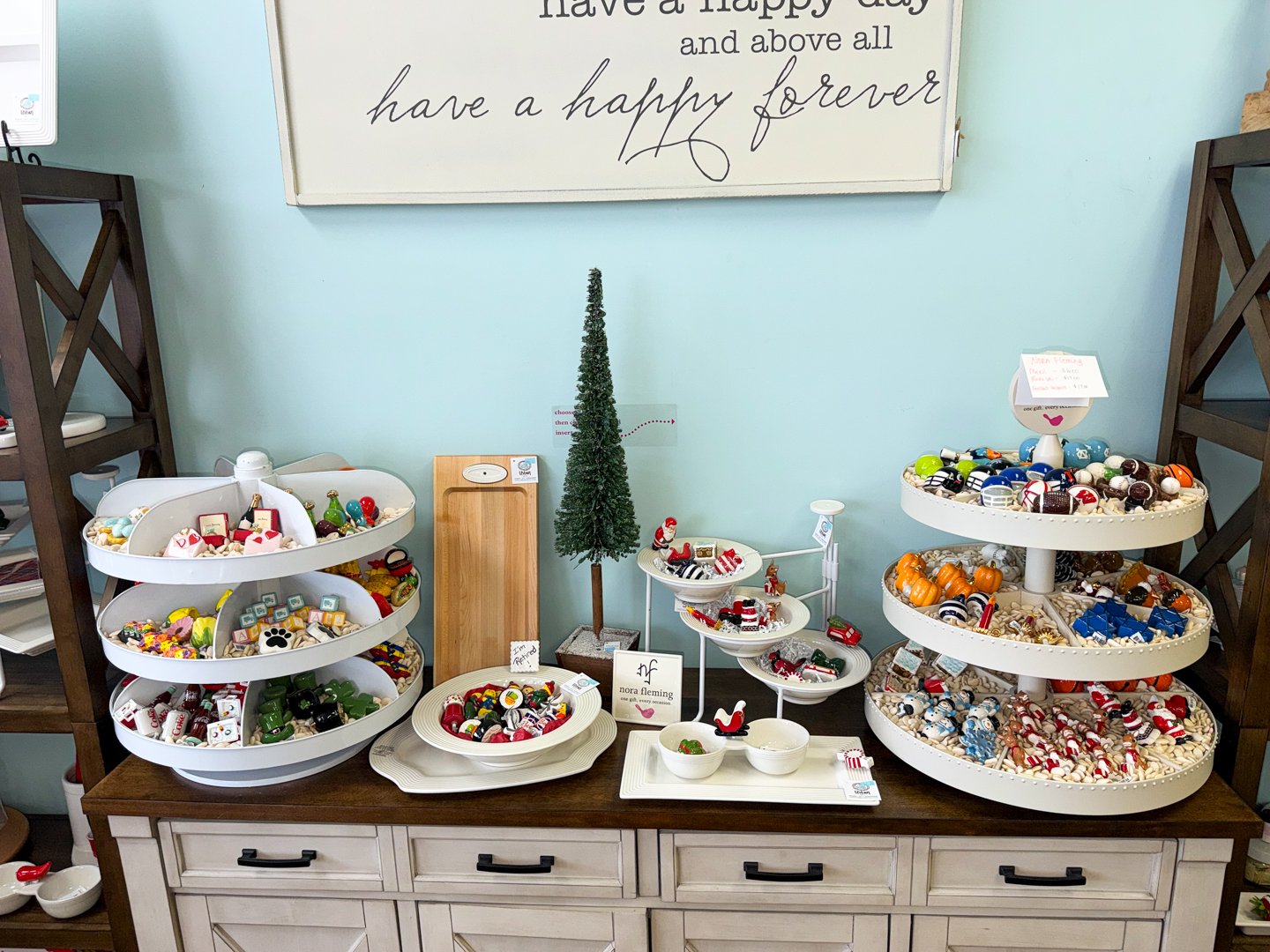 Display of Nora Fleming serving ware and decorative minis, featuring versatile platters and seasonal toppers