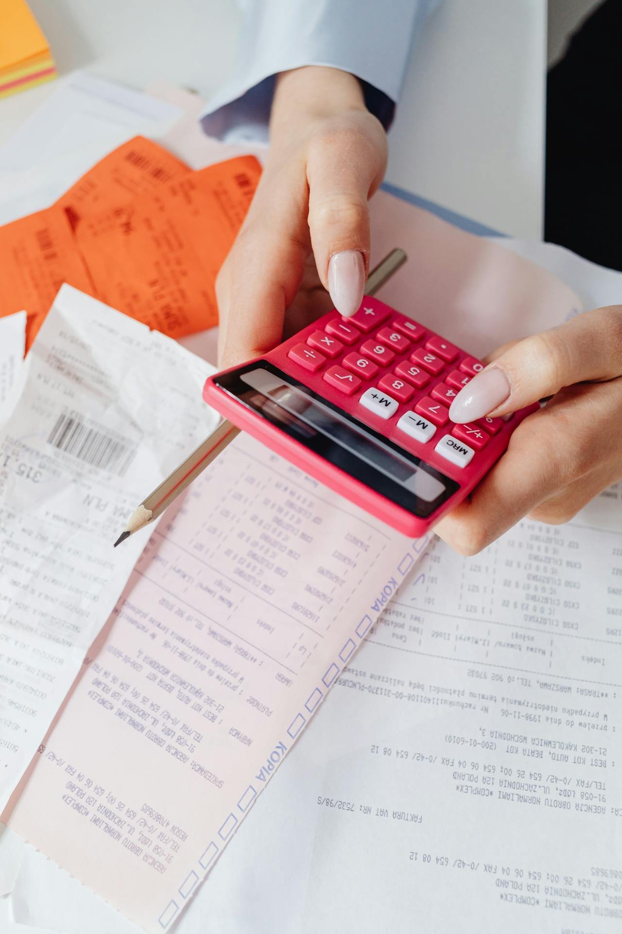 Woman using a red calculator and holding a pencil.