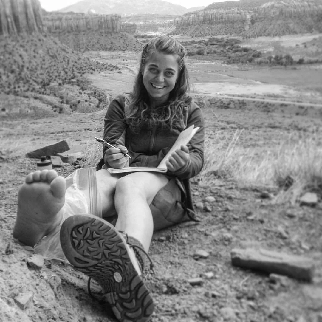 Erin sits in Indian Creek, traditional territory of the Navajo, Hopi, Zuni, Ute Mountain Ute, & Uintah Ouray Ute tribes, a few years ago nursing her freshly sprained ankle.