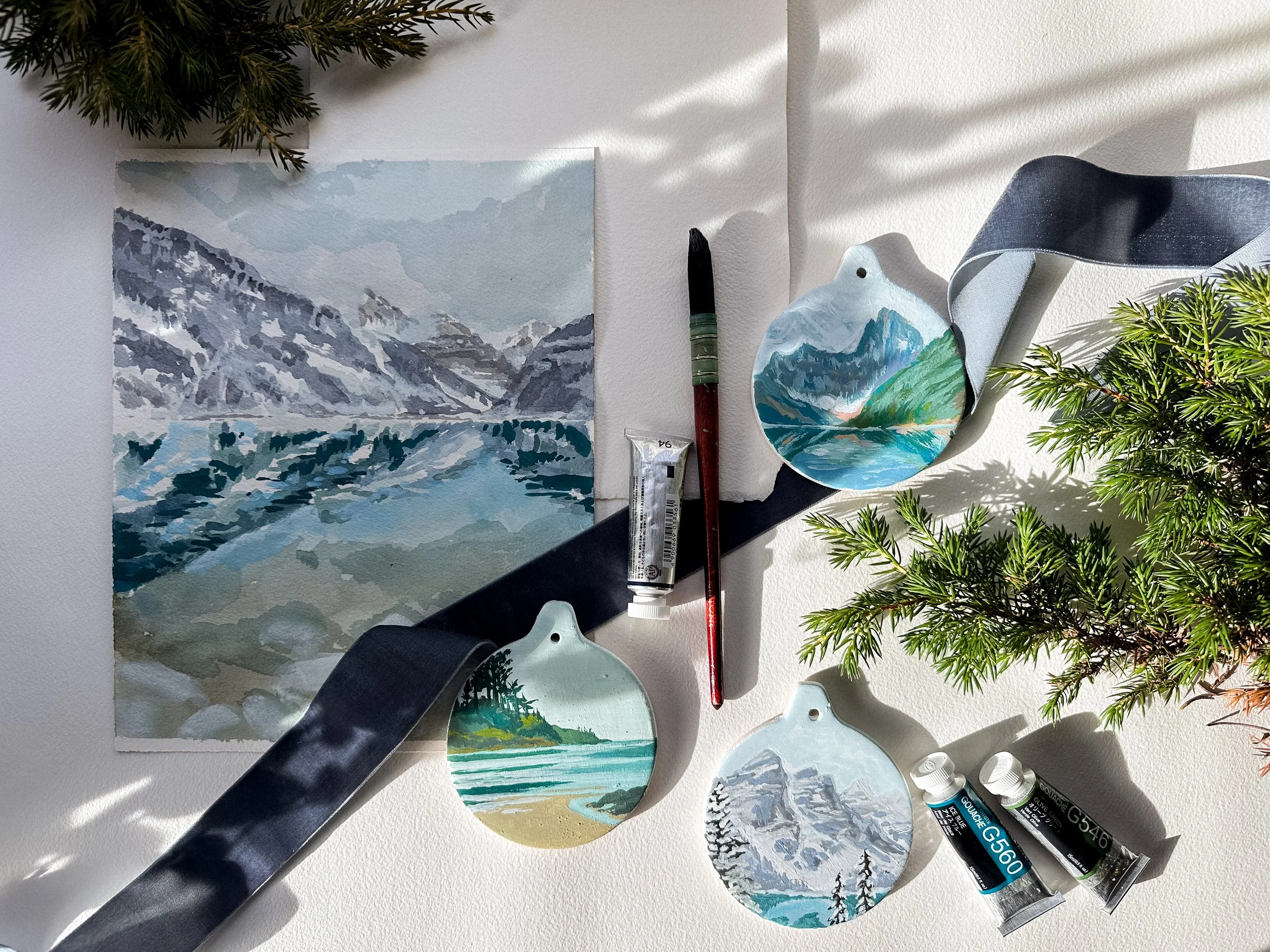 a collection of hand painted landscape ornaments with an original painting of Lake Louise in winter