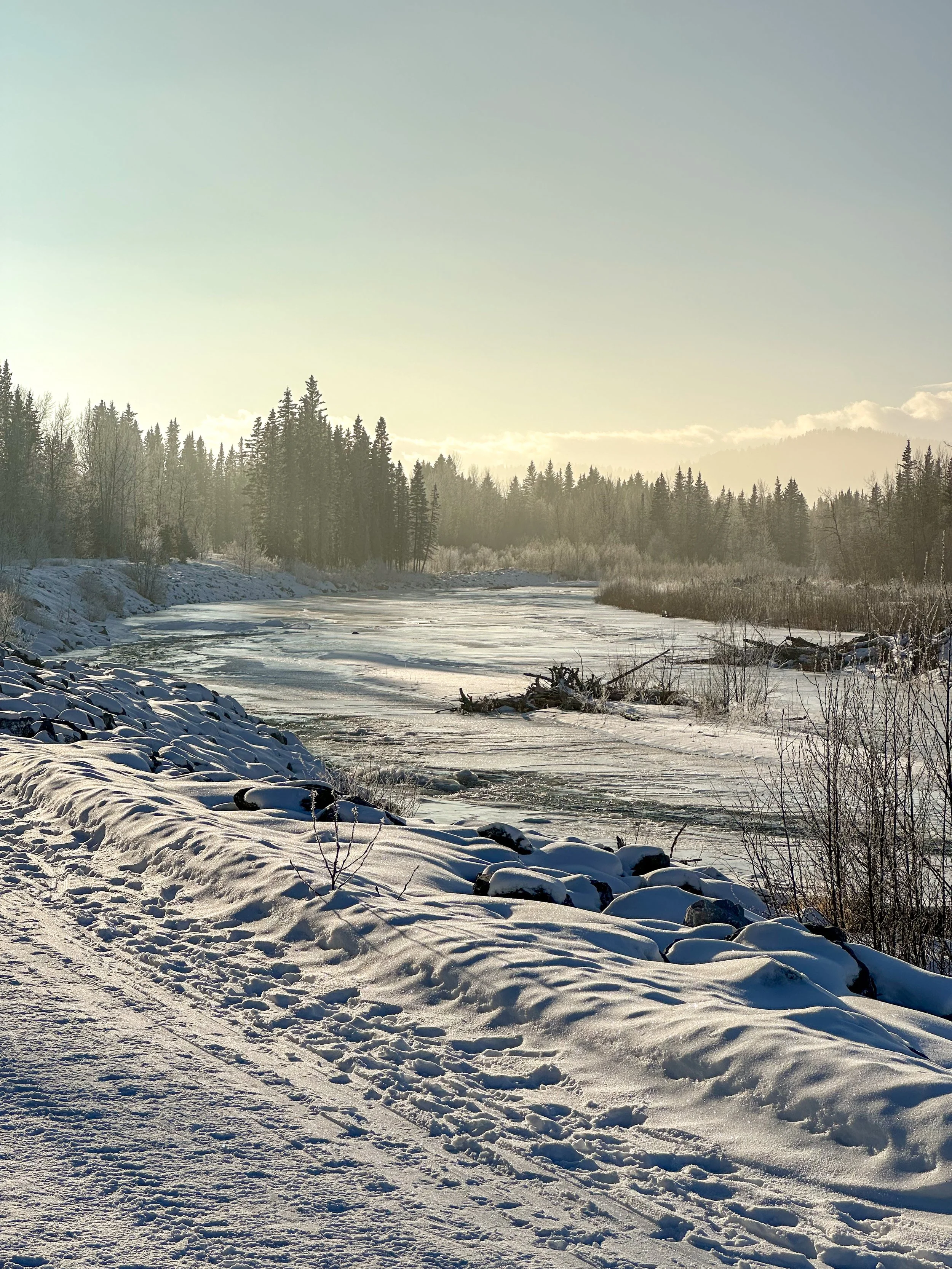 Winter in Redwood Meadows along the frozen Elbow River with a golden hazy sky