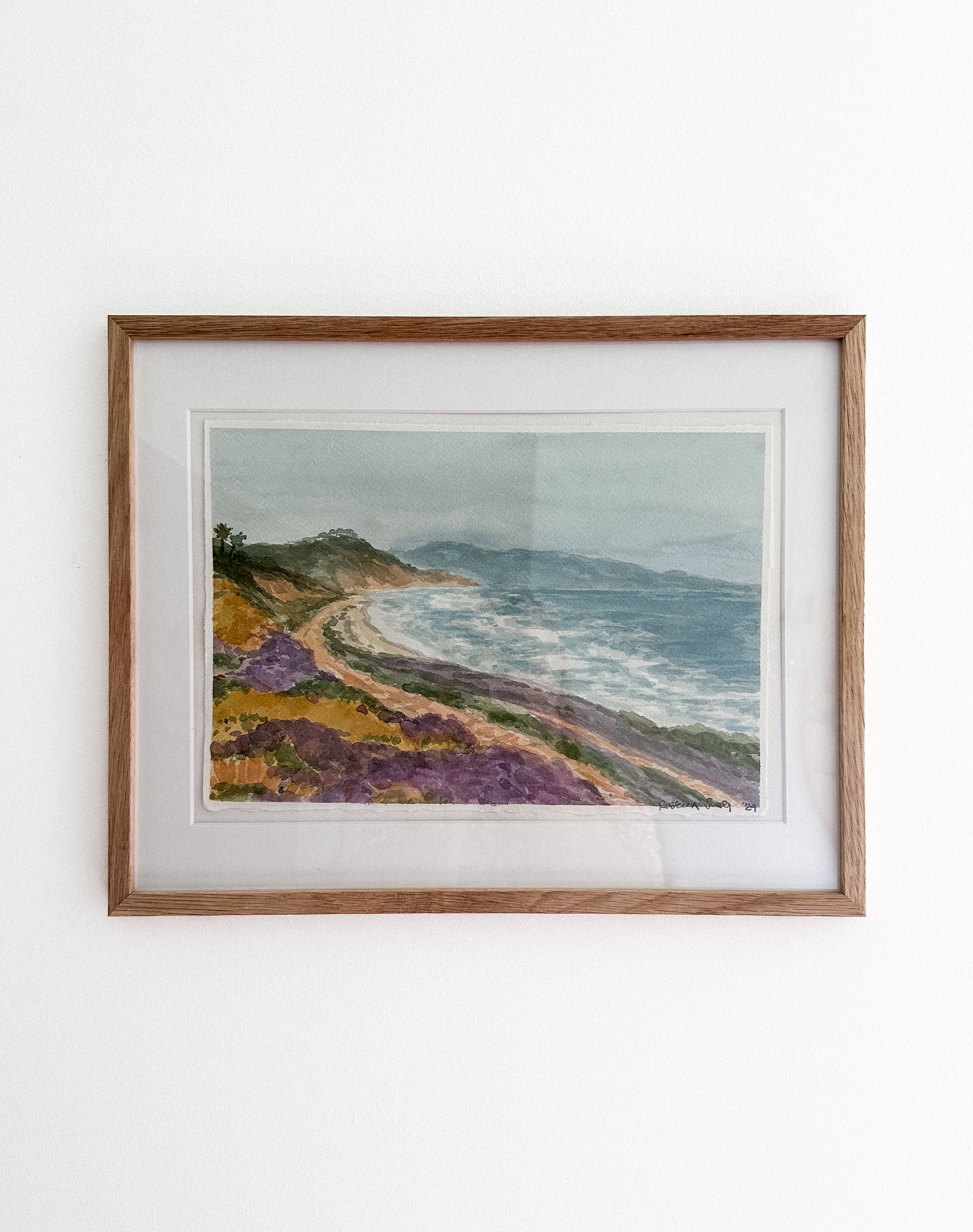 Framed watercolor landscape painting of purple and yellow wildflowers lining a coastal cliff overlooking Torrey Pines Beach in Del Mar, California