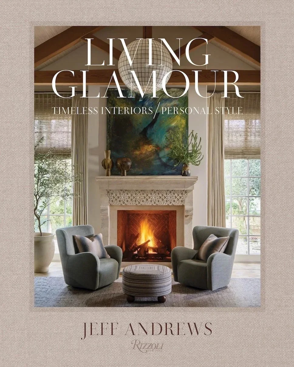Jeff Andrews' book cover for Living Glamour: Timeless Interiors/Personal Style published by Rizzoli including a warm fireplace with cream mantle in a high ceilinged room with vaulted beams two cozy chairs with a textured ottoman between them