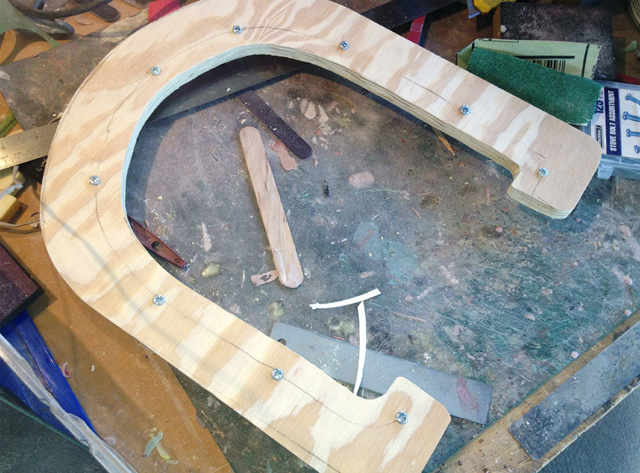  I cut two pieces of 1/4″ plywood to make a parting line for the mother mold. This was placed over the center of the helmet and Plasti-Paste II was applied on each side to support the mold rubber. 