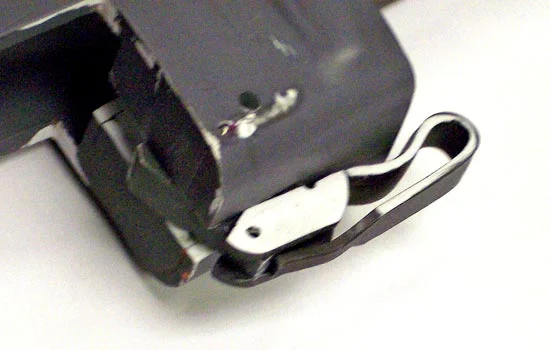 The latch in position shows how the latch rotates and, with pressure from a hidden spring, locks the magazine in place. The folding handle flips down and then moves the latch away from the magazine, allowing it to be removed.