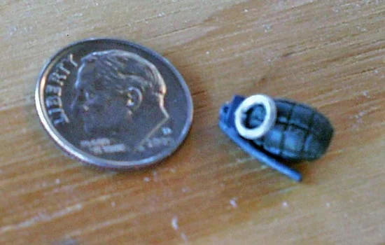 The grenade was formed from Aves with a nail stuck in it. When it was dry, I stuck the nail in a drill and lathed in the horizontal grooves. I attached small styrene blocks for the upper part of the grenade. The grenade ring was made from round styrene bar stock. I heated the plastic and wound it around a brass tube. I snipped off one link and then glued it closed. The “handle” of the grenade was made from a sliver of aluminum.