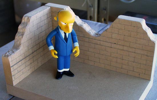 I cut the base and walls from 1/2″ MDF to match the dimensions of the other World of Springfield line. The broken bricks were roughed in using the Dremel.