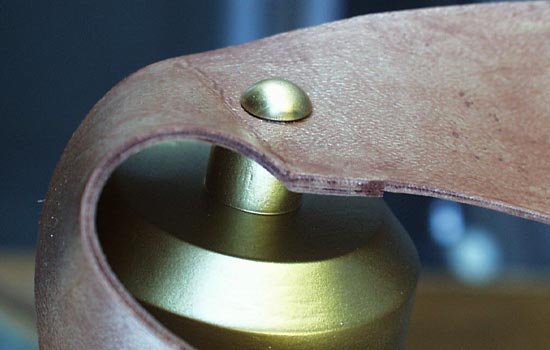 A .625″ dowel was screwed onto the cap (before it was glued on) and the the strap was epoxied to the dowel. I painted an upholstery tack with the same gold paint and attached it to the inside.