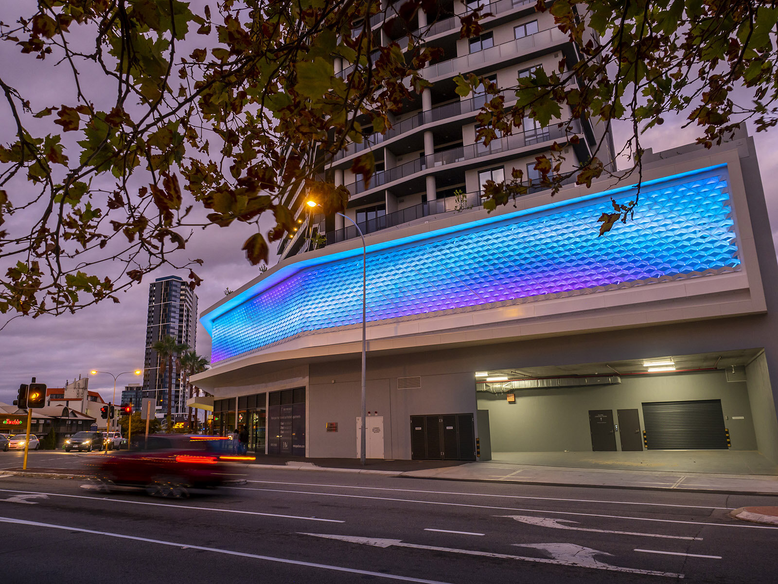 Undulation & Flow, 2016-20. The Precinct apartments, Mt Pleasant, WA. Podium facade cladding screen, featuring coloured programmed lighting. Materials: powdercoated white aluminium sheet, arrayed in a folded and welded diagrid, plus Philips C