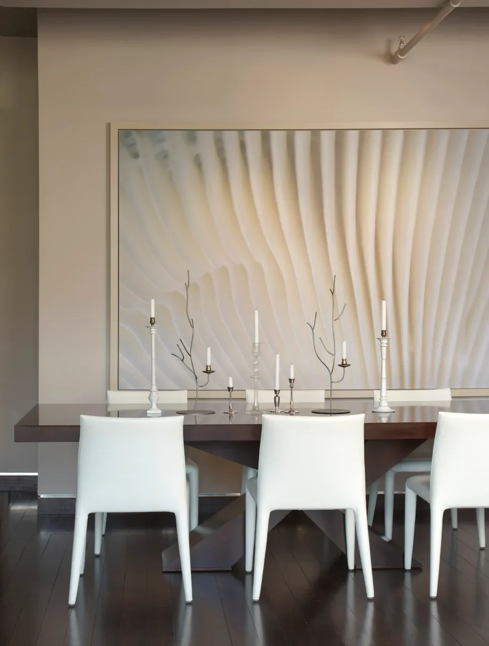Modern dining room with a dark wood table, white chairs, and a large abstract artwork on the wall featuring soft, flowing lines.