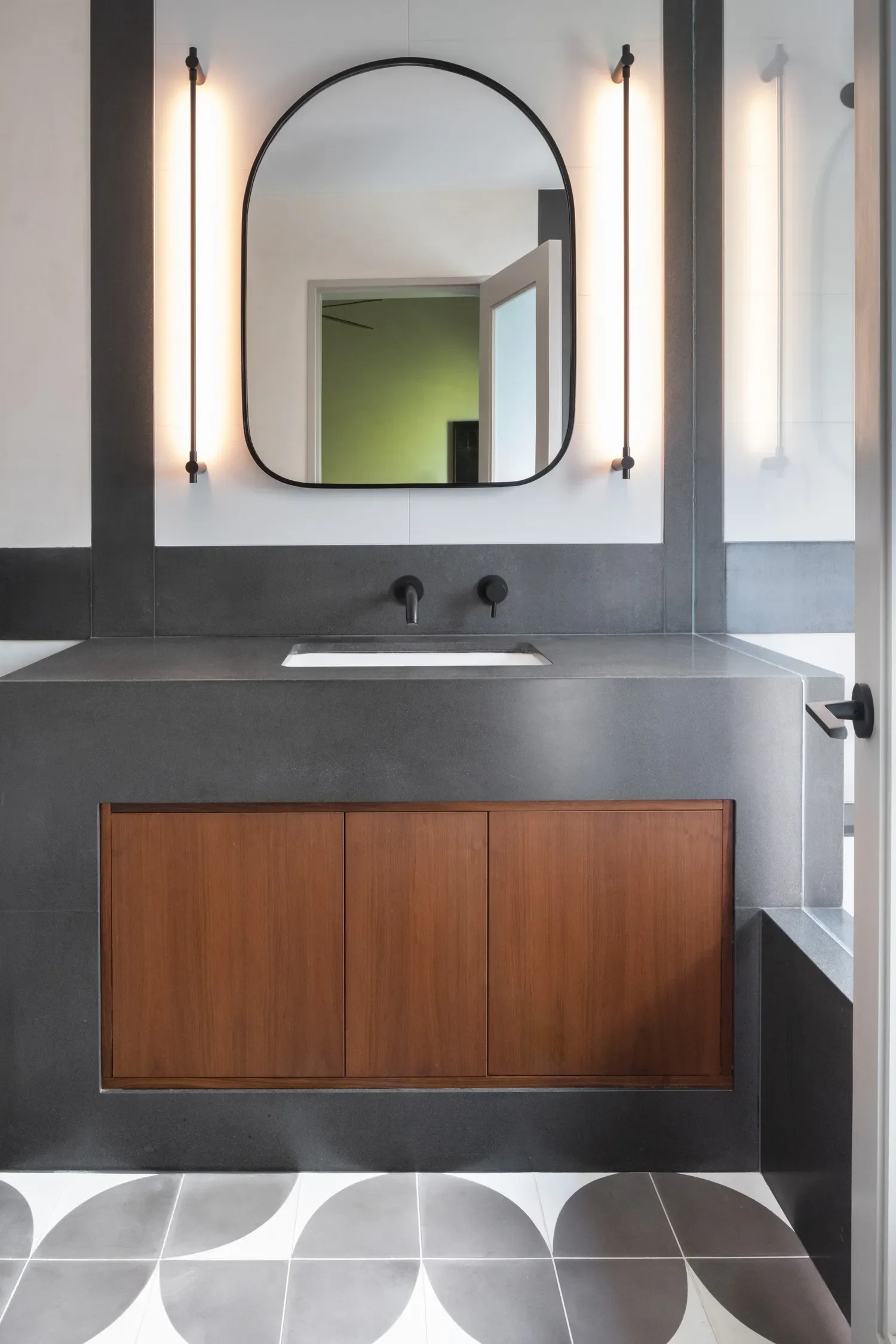  In this bathroom, a cold gray monolithic vanity is warmed by inset walnut doors. The curvilinear mirror and floor tile graphic counterbalance an abundance of straight lines.