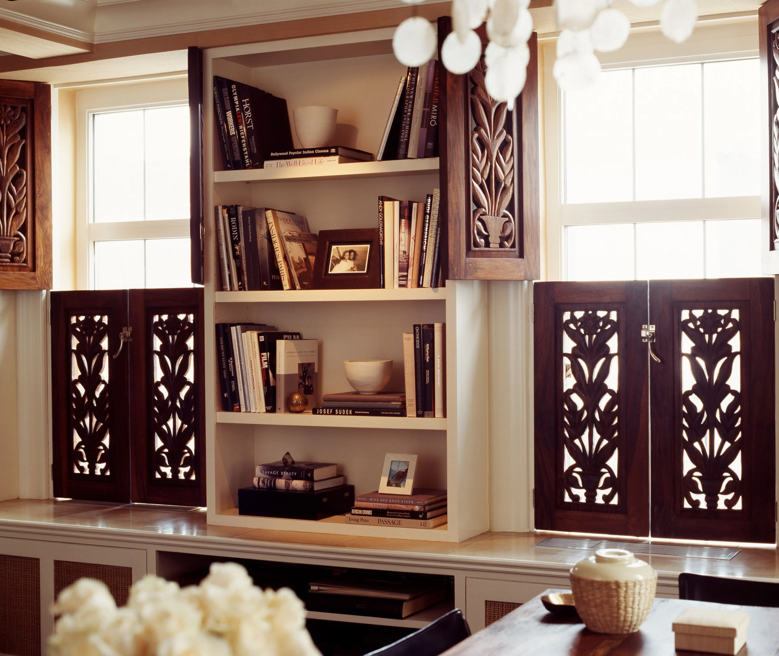 Built-in bookshelves framed by ornate carved wood shutters displaying books, photos, and ceramics