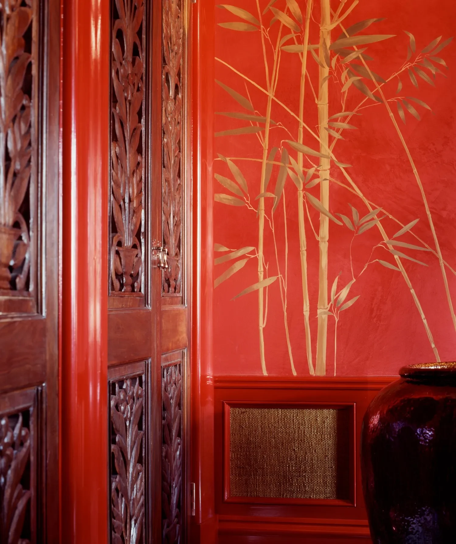 Decorative interior corner with wooden lattice doors, red walls, bamboo plant mural, and a dark glossy vase.