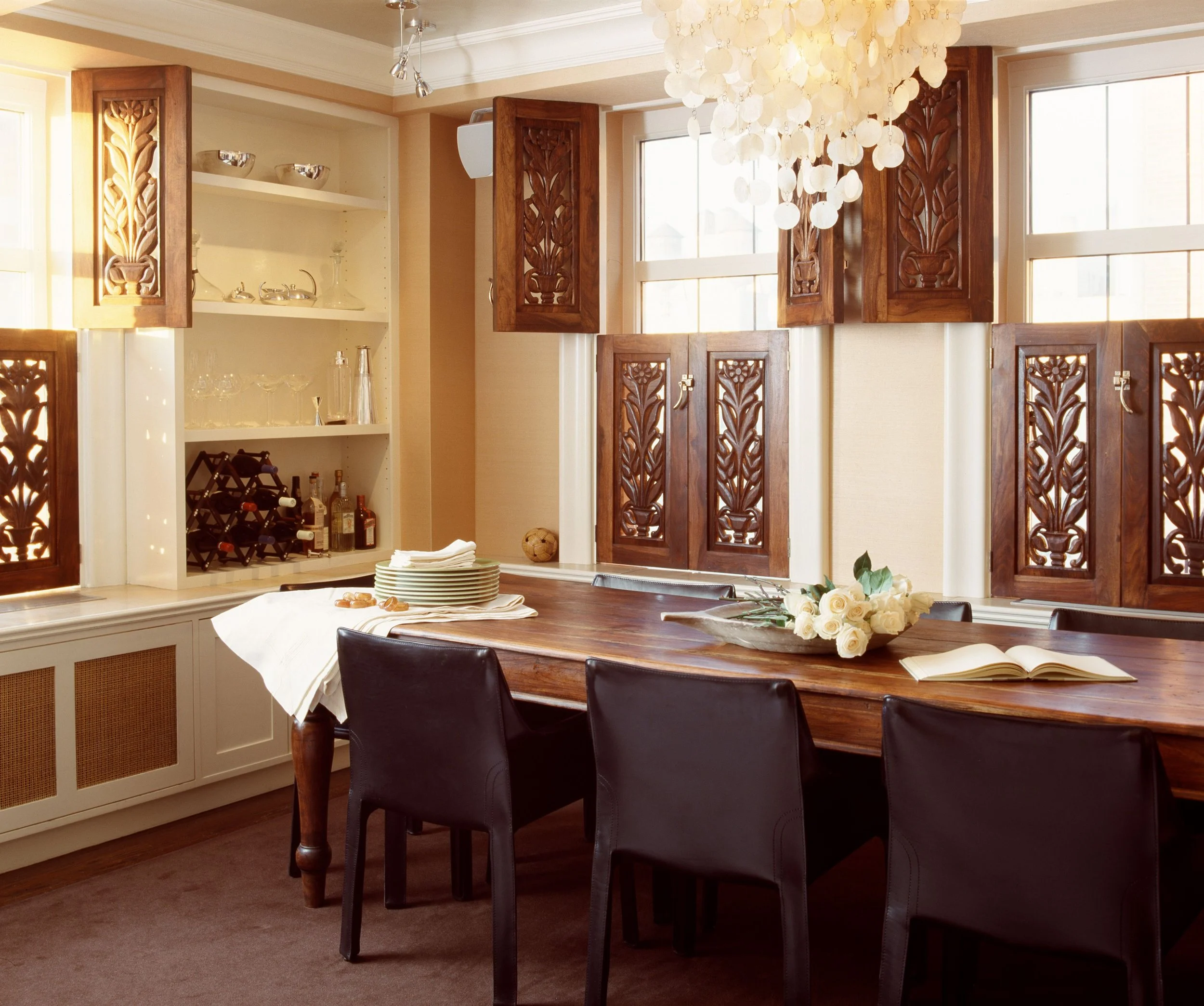 Elegant dining room with carved wood shutters, capiz chandelier, and walnut table with white roses