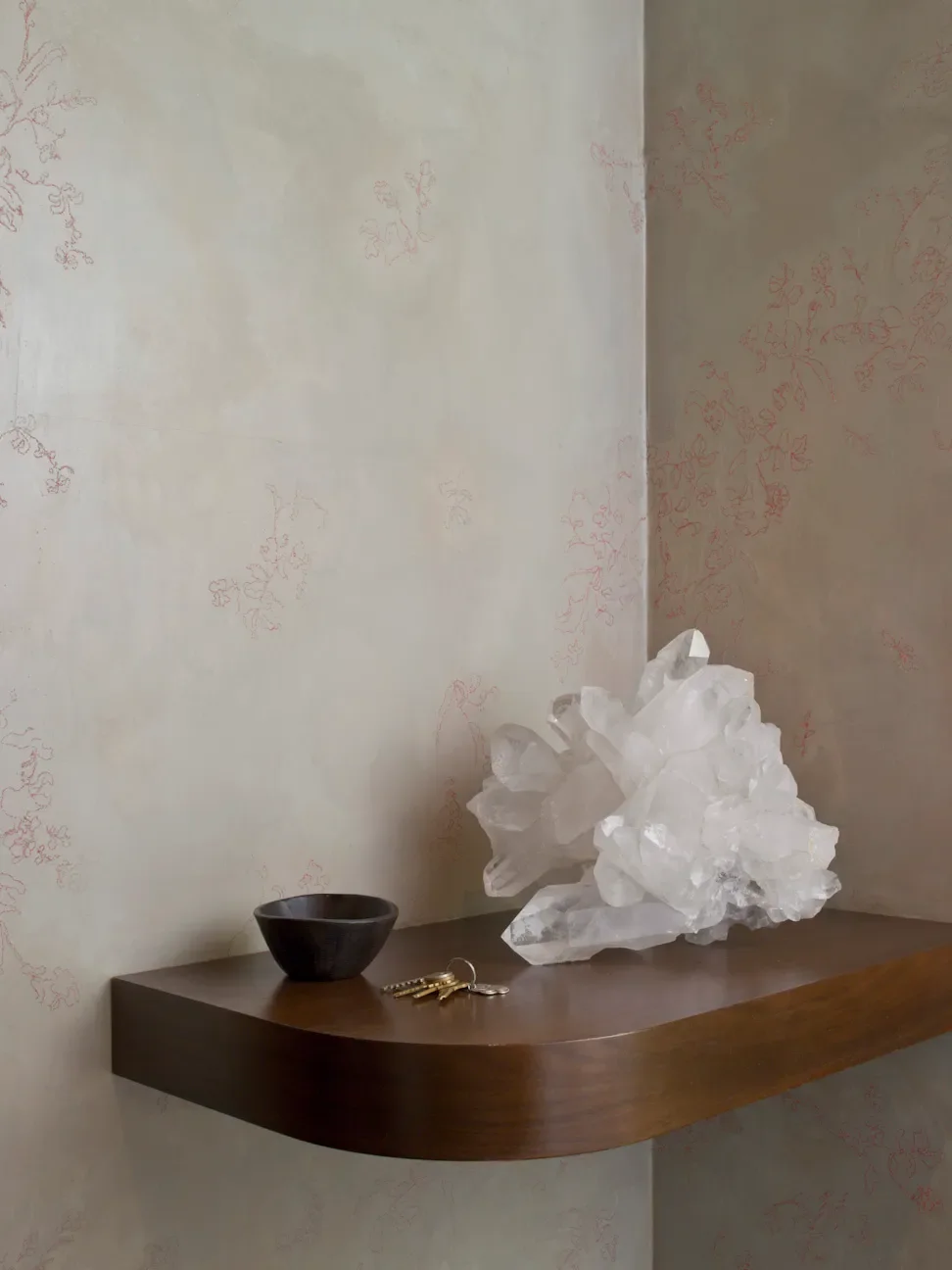 Decorative display on a wooden wall shelf with a large clear quartz crystal cluster, a small black bowl, and a set of keys with keychains.