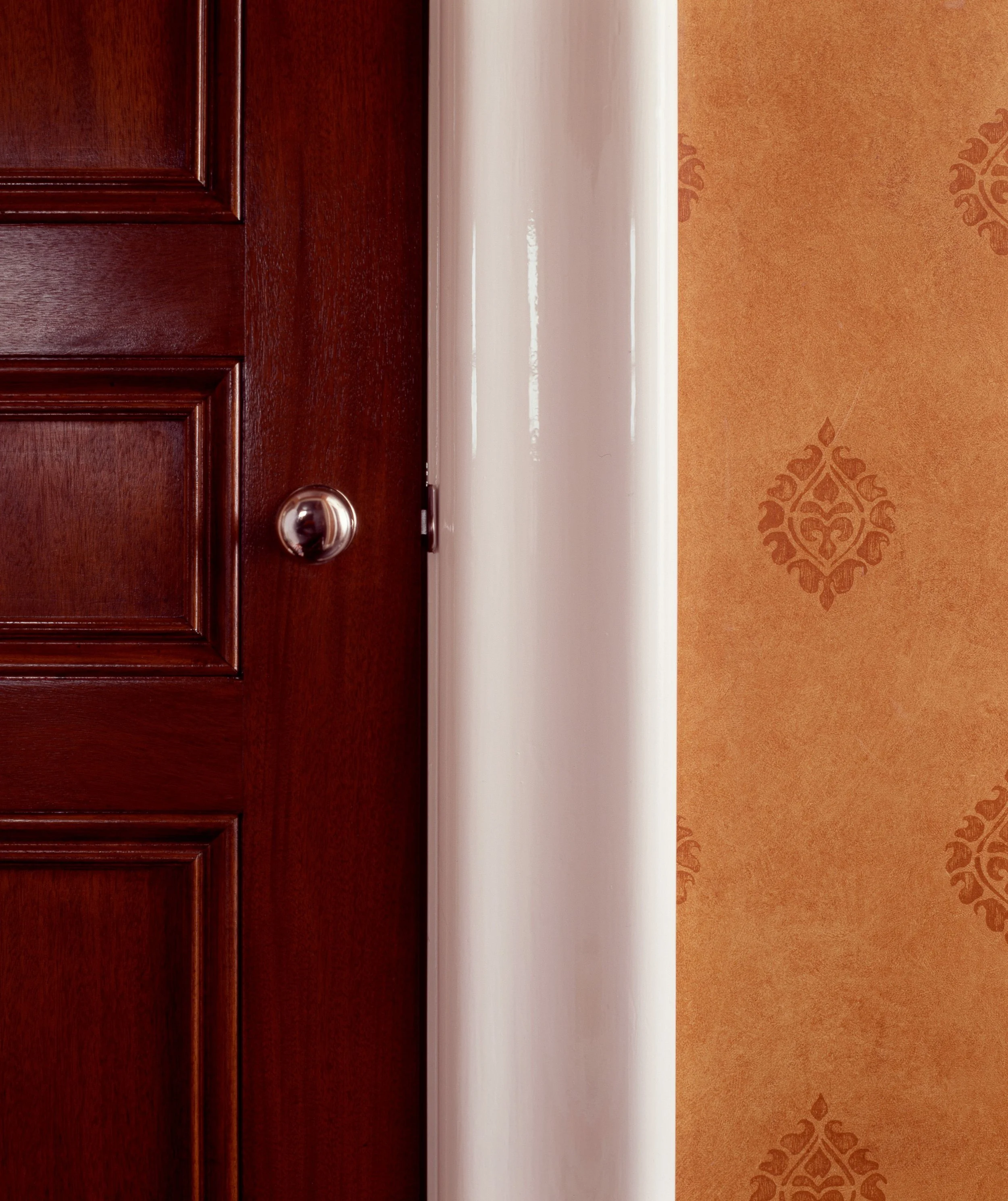 Rich mahogany paneled door beside warm gold damask wallpaper with white trim detail
