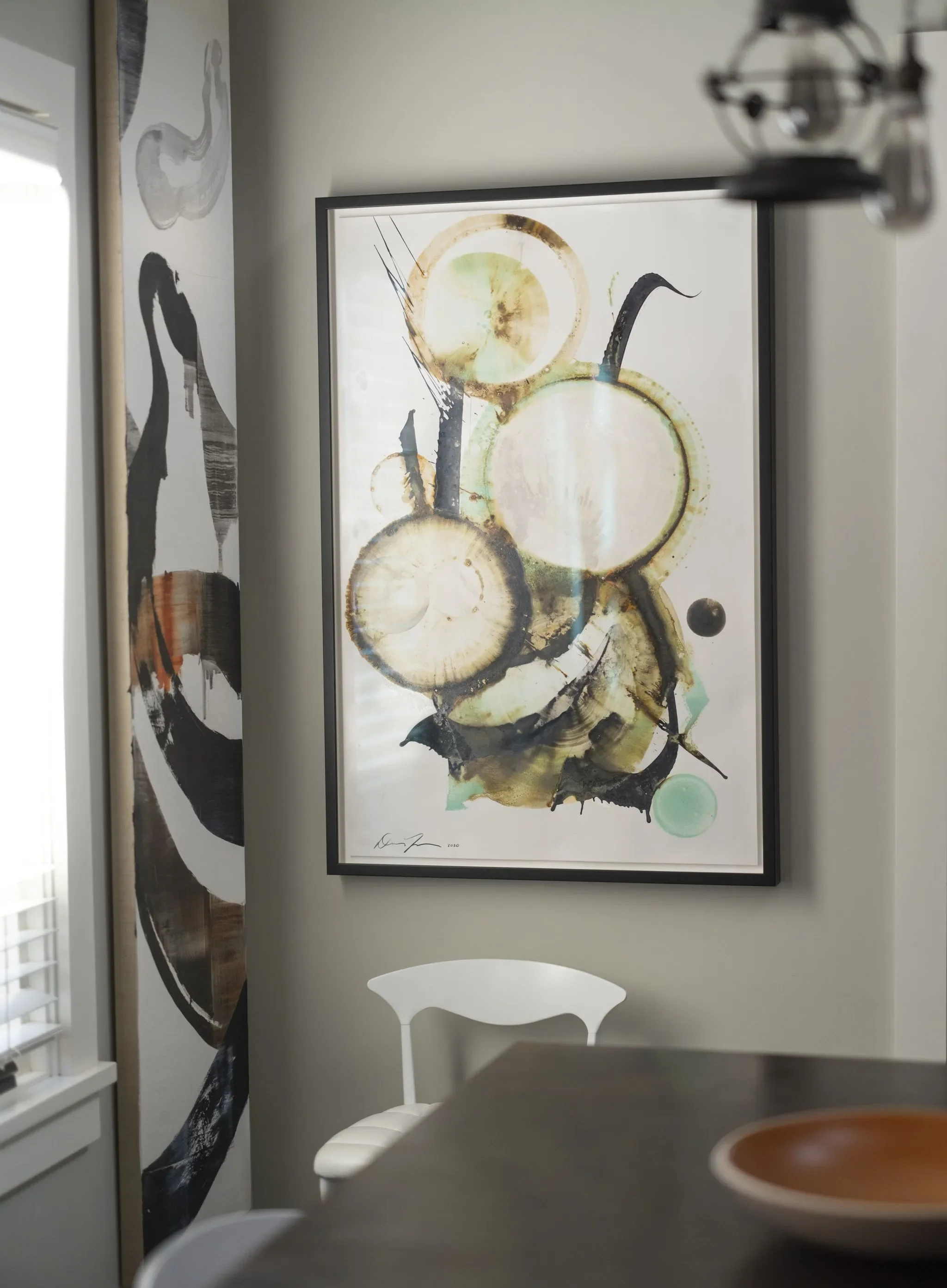 Abstract watercolor painting of overlapping circles in shades of yellow, green, black, and brown, displayed on a white wall.