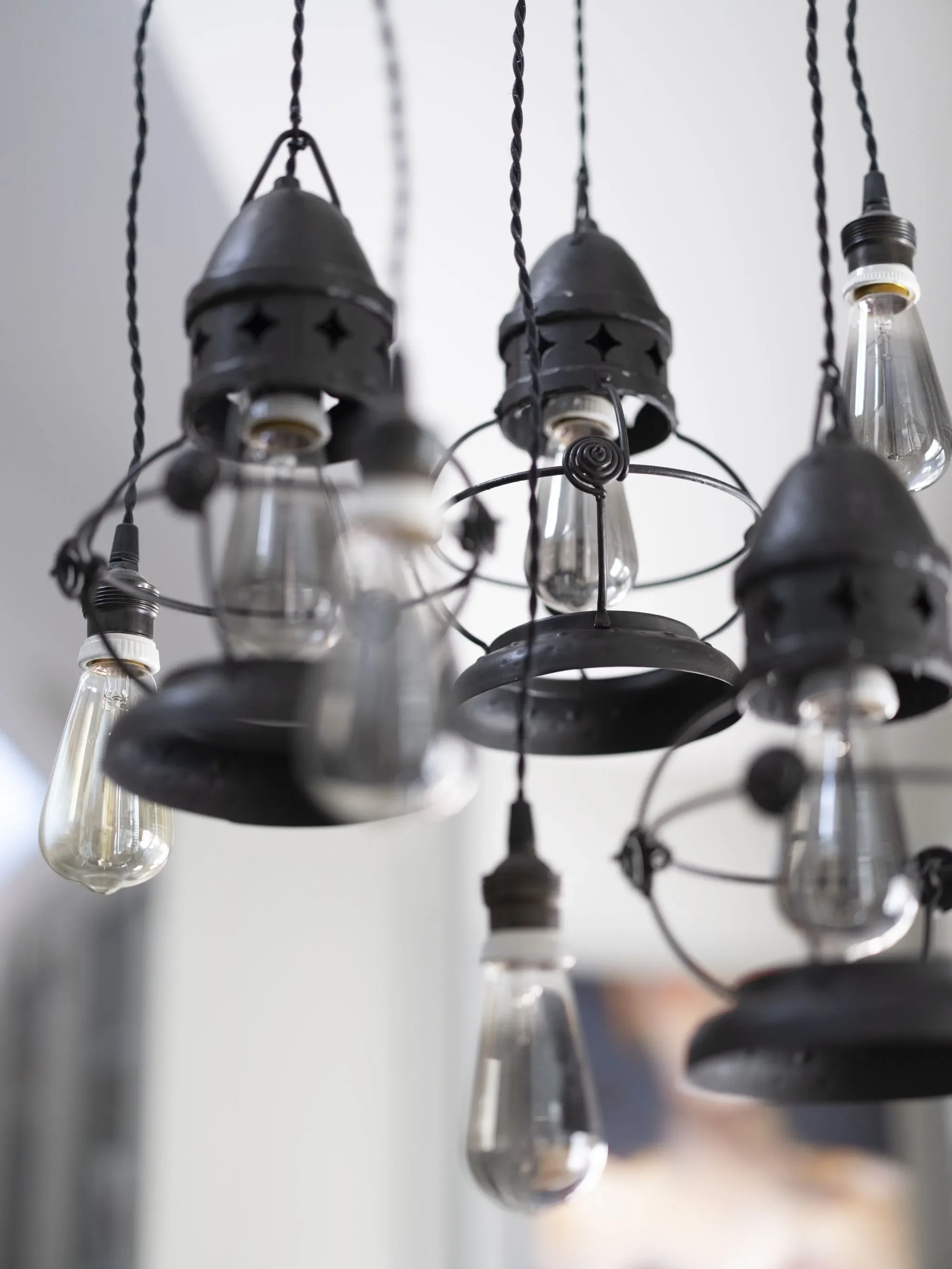 A close-up view of a chandelier with hanging light bulbs and black metal fixtures against a white background.