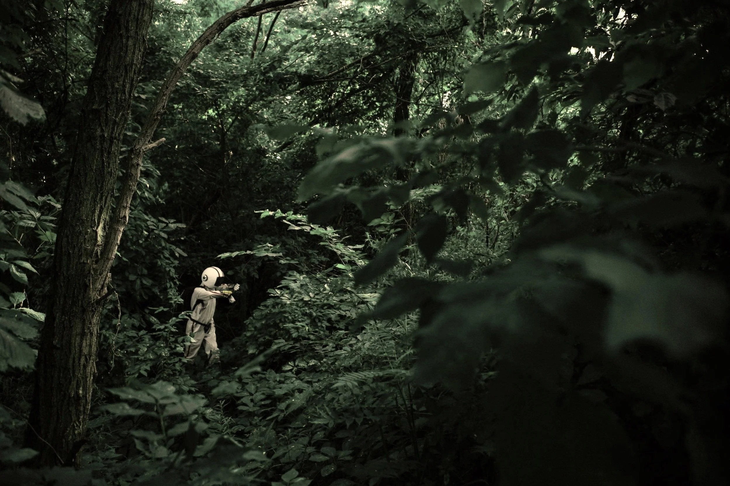 A person wearing a helmet and outdoor clothes walking through a dense forest with lush green foliage.