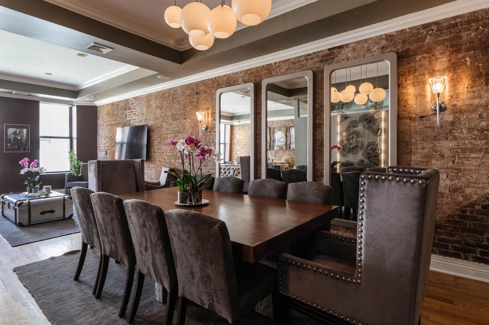 Dining room area with long wooden table and brick wall with hanging mirrors