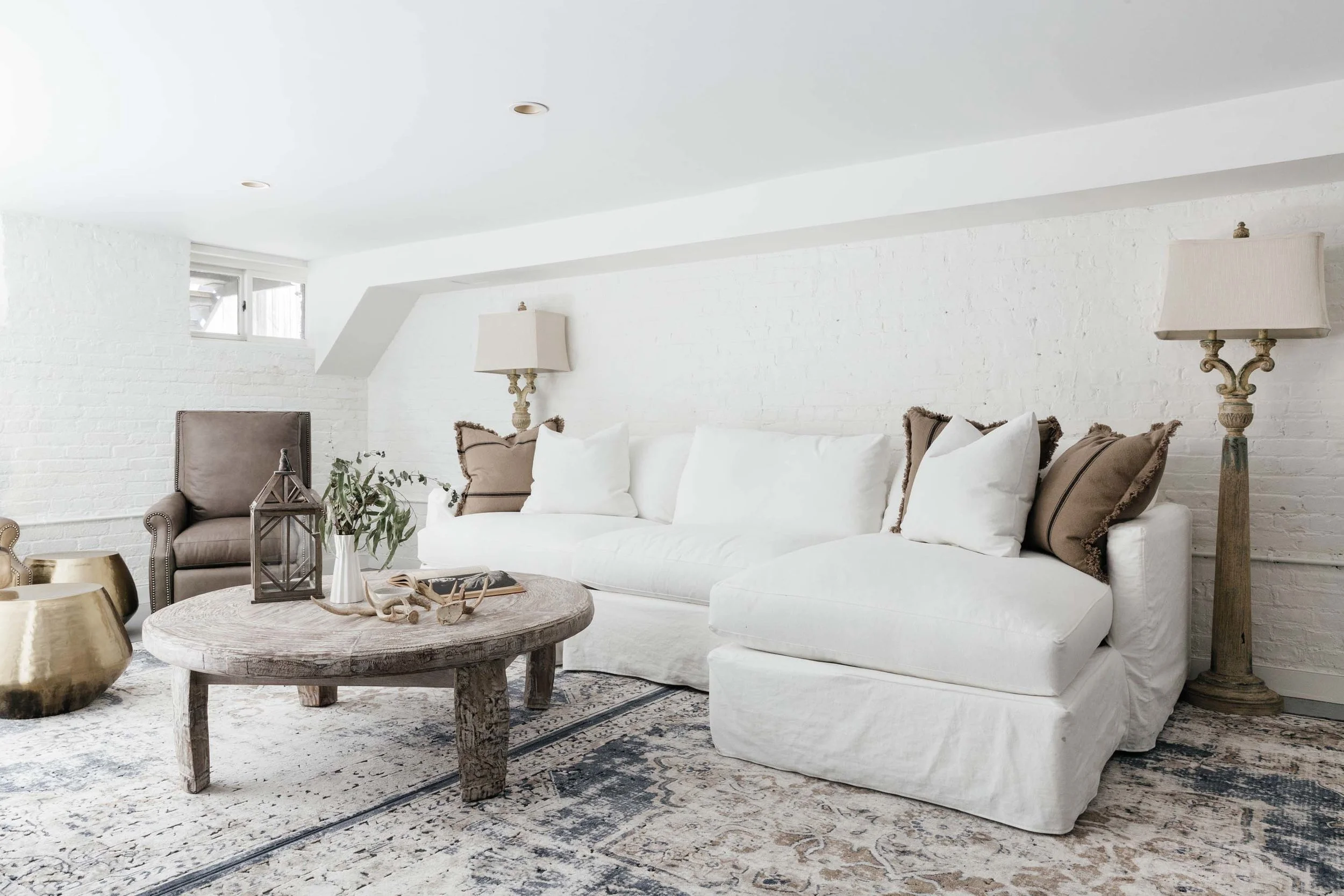 Bright basement seating area with white sectional sofa and rustic brown coffee table