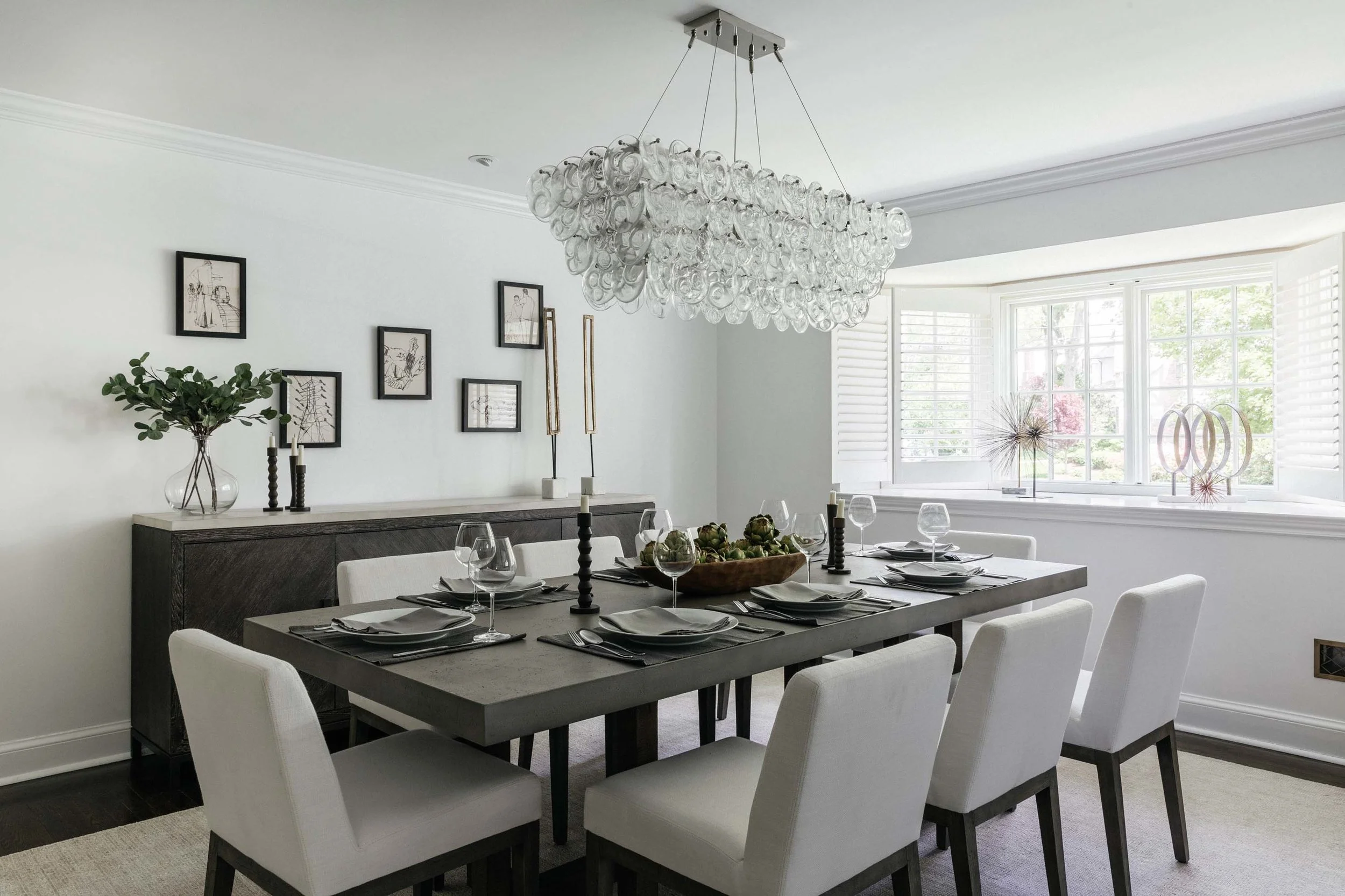 Dining room with dining table, plates, wine glasses, white painted walls and modern chandelier