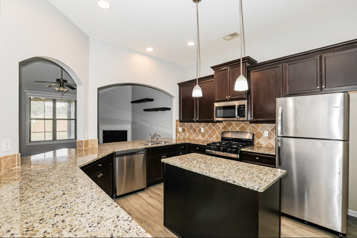 Modern kitchen with granite countertops, dark wood cabinets, stainless steel appliances, and pendant lighting. Photographed by Branded by MDM 