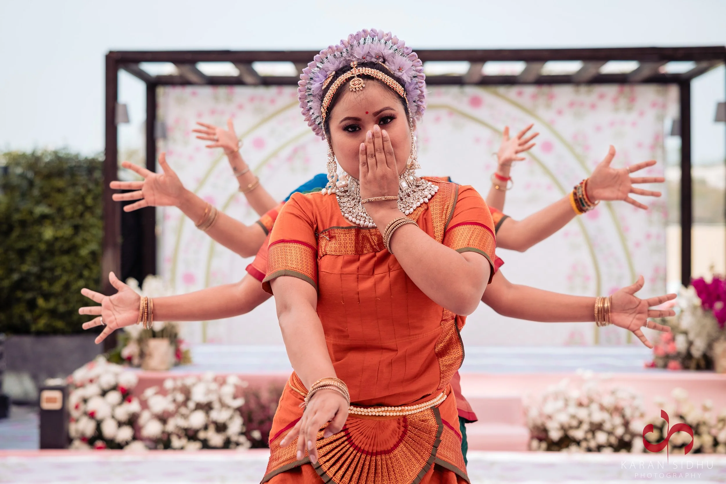 A woman dressed in traditional Indian attire performing a dance with four additional arms attached, during a cultural event or performance.