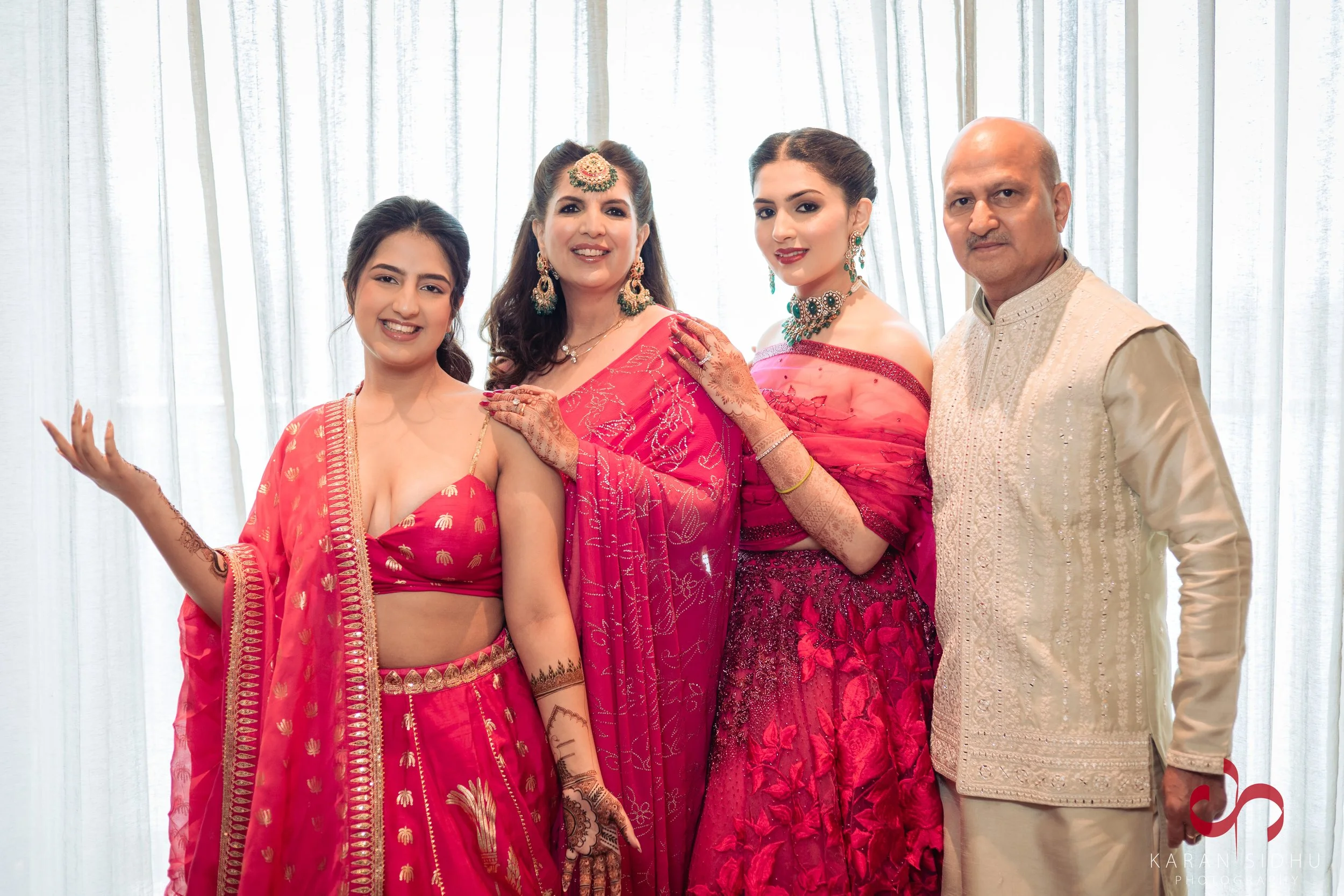 Family of four dressed in traditional Indian attire standing together in front of a white curtain.