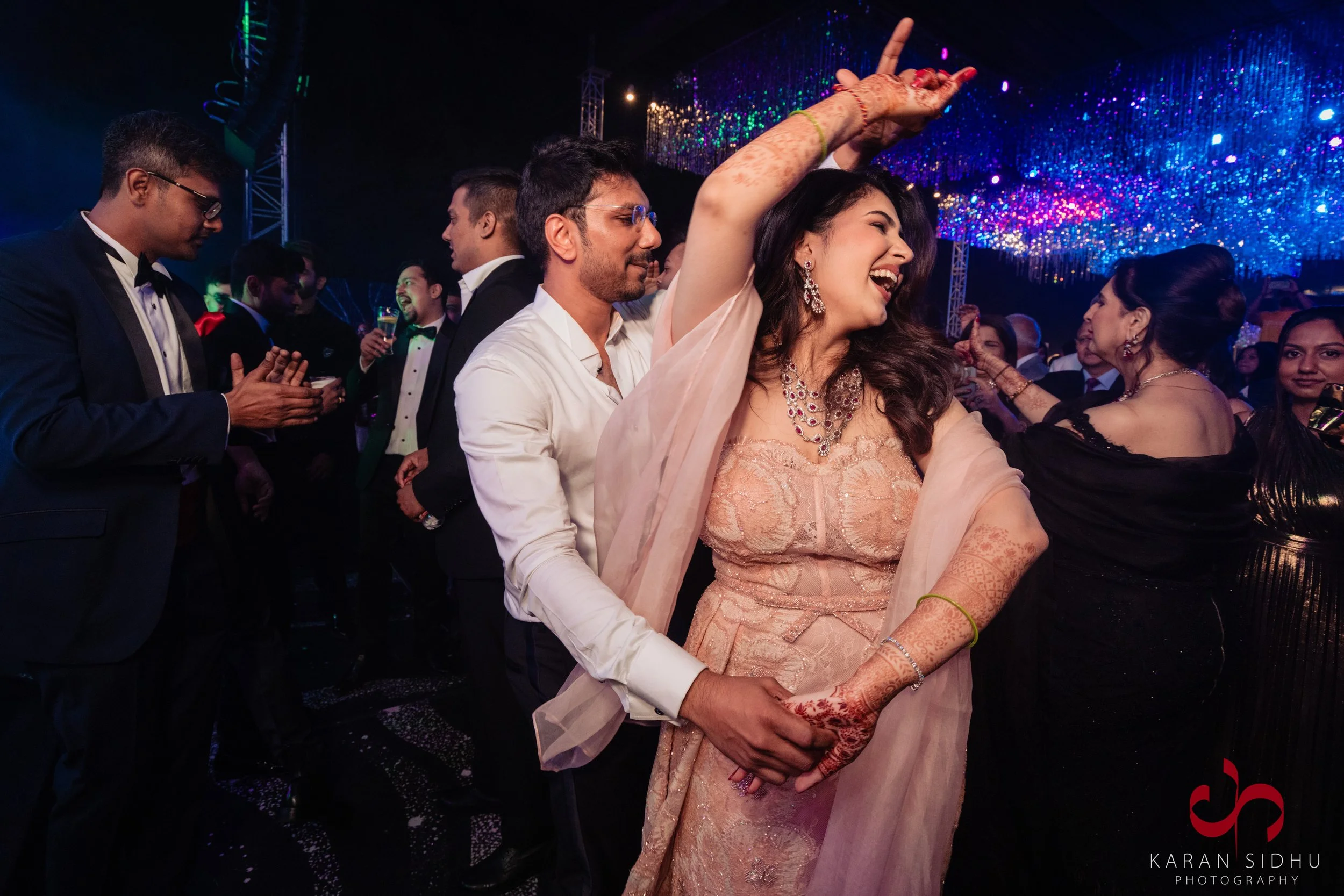 People dancing and celebrating at a party with colorful lights in the background.