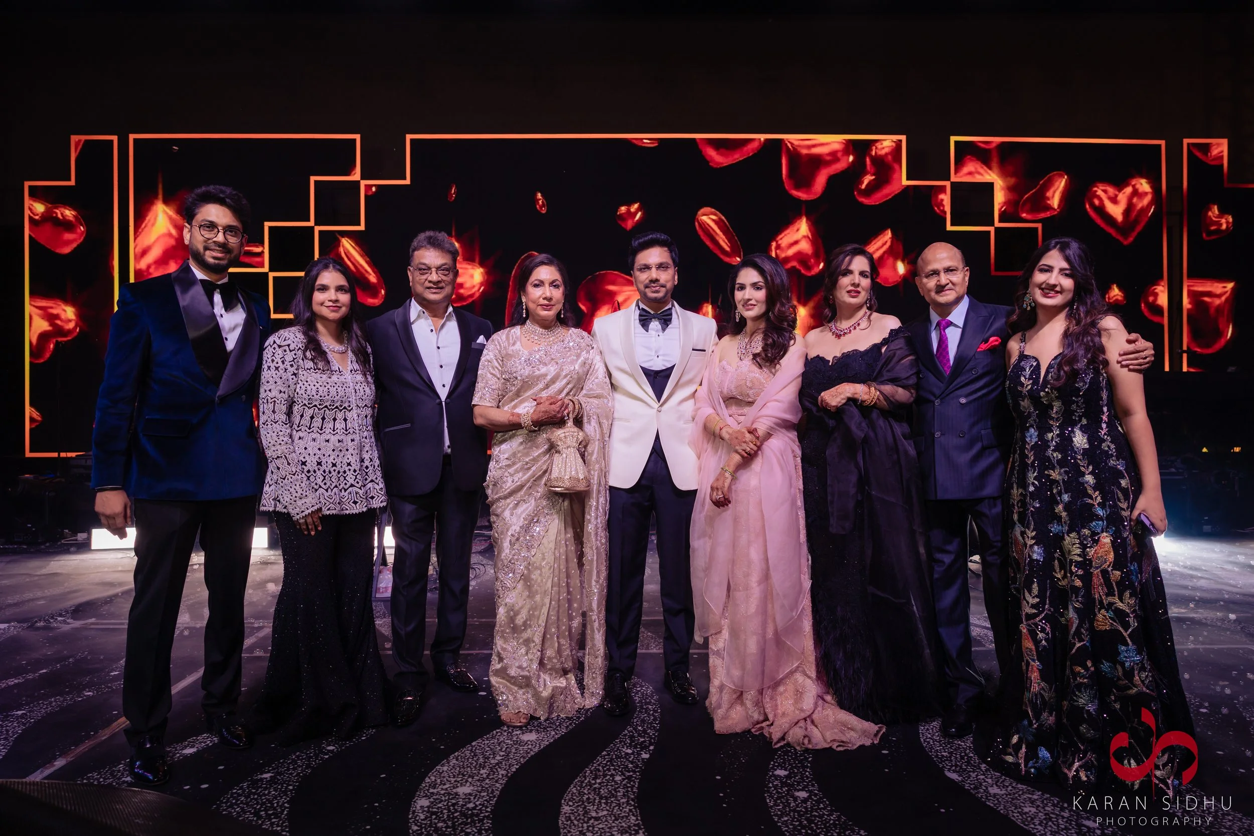 Group of ten people dressed in formal attire standing on stage with a digital display of red heart shapes in the background.