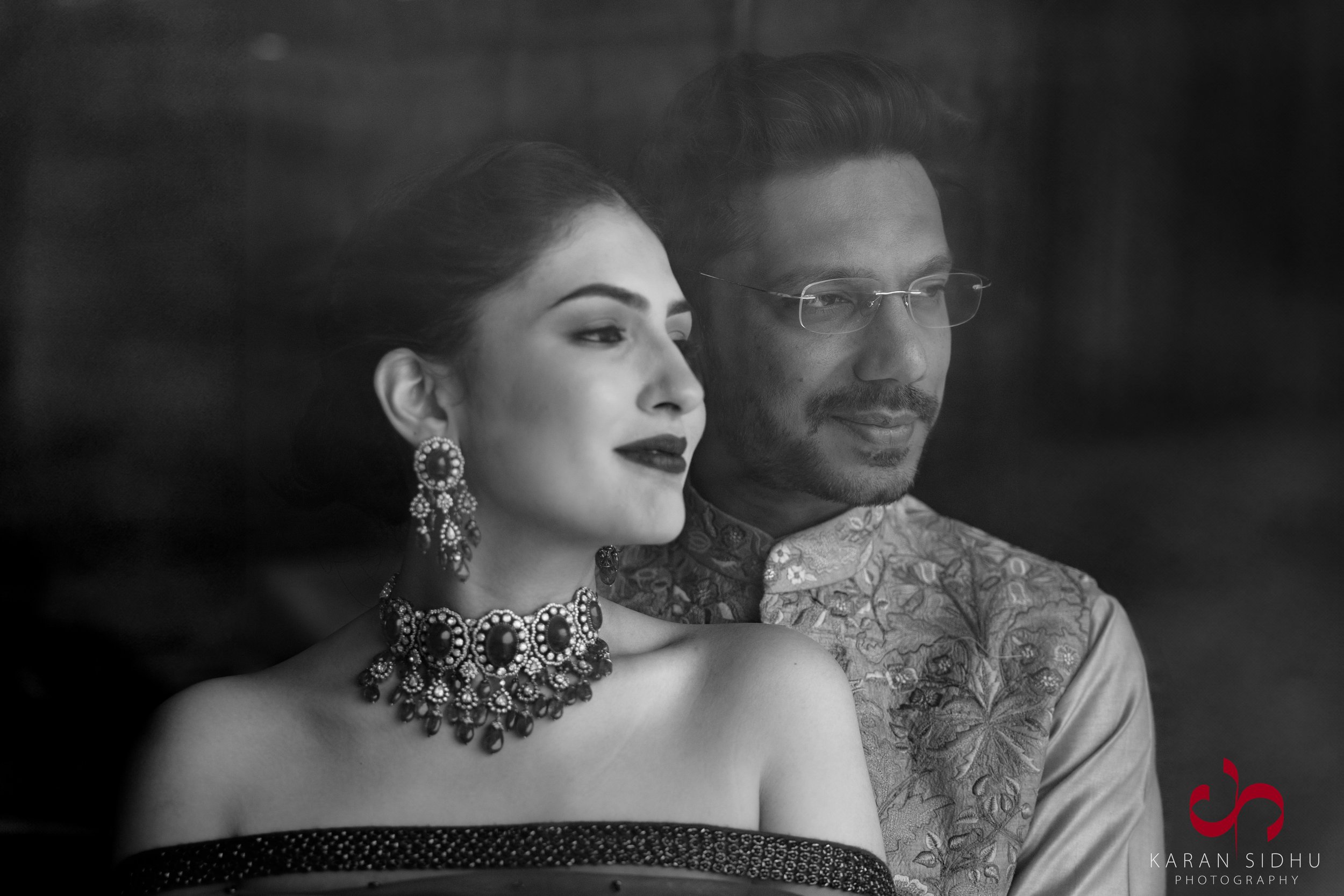 A black and white portrait of a man and woman dressed in traditional Indian attire, gazing out a window.