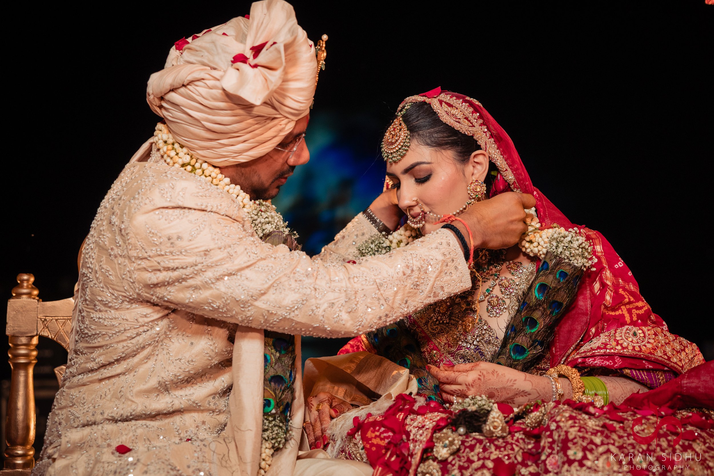 Indian bride and groom during a wedding ceremony, with the groom adjusting the bride's jewelry.
