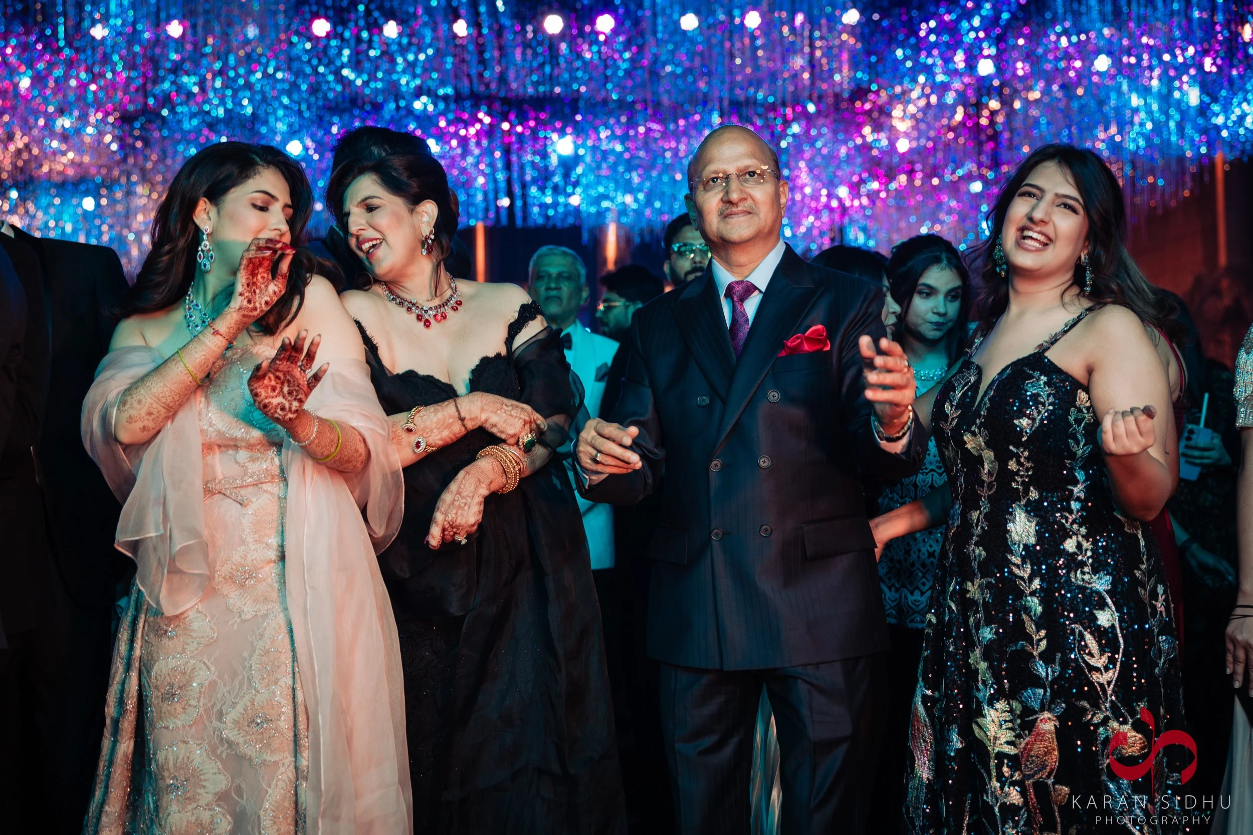 Group of people dressed in formal attire at an indoor event with colorful lighting and decorations.