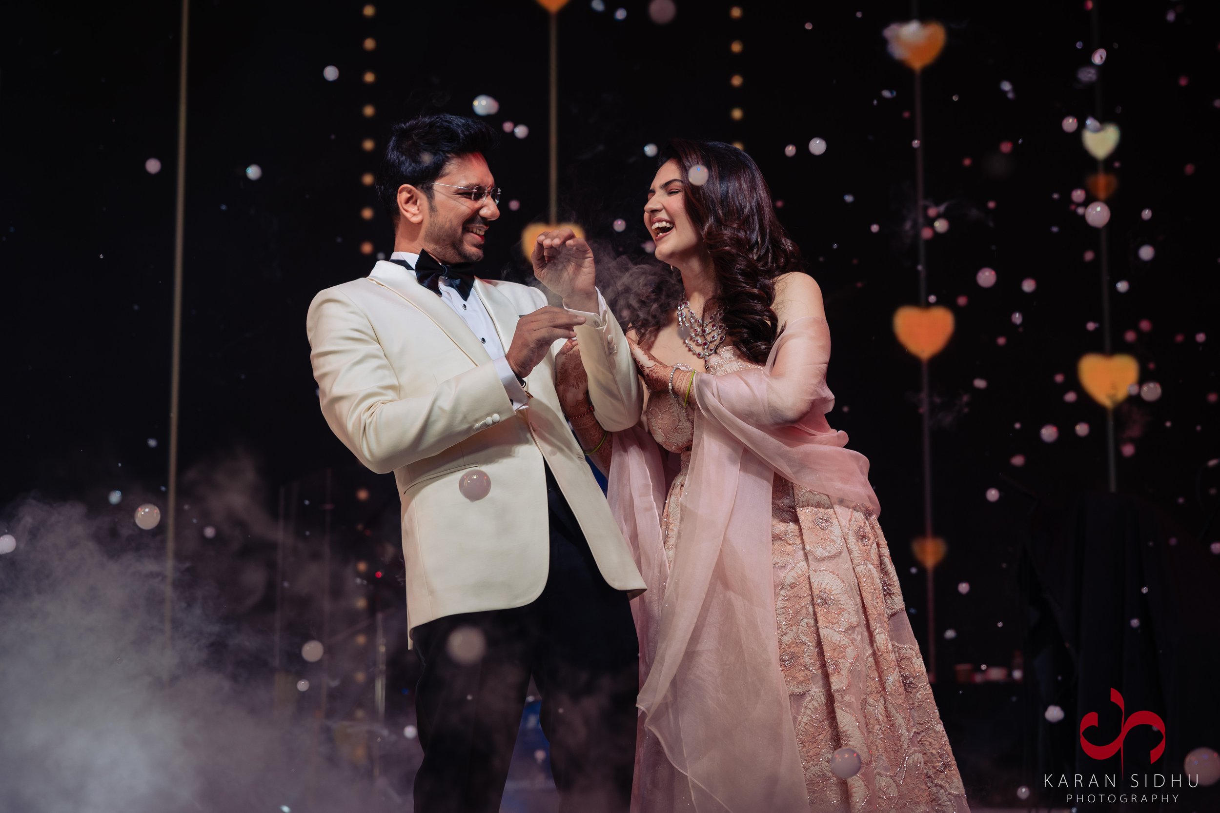 A newlywed couple celebrating at their wedding reception, smiling and looking happy with love-themed decorations in the background