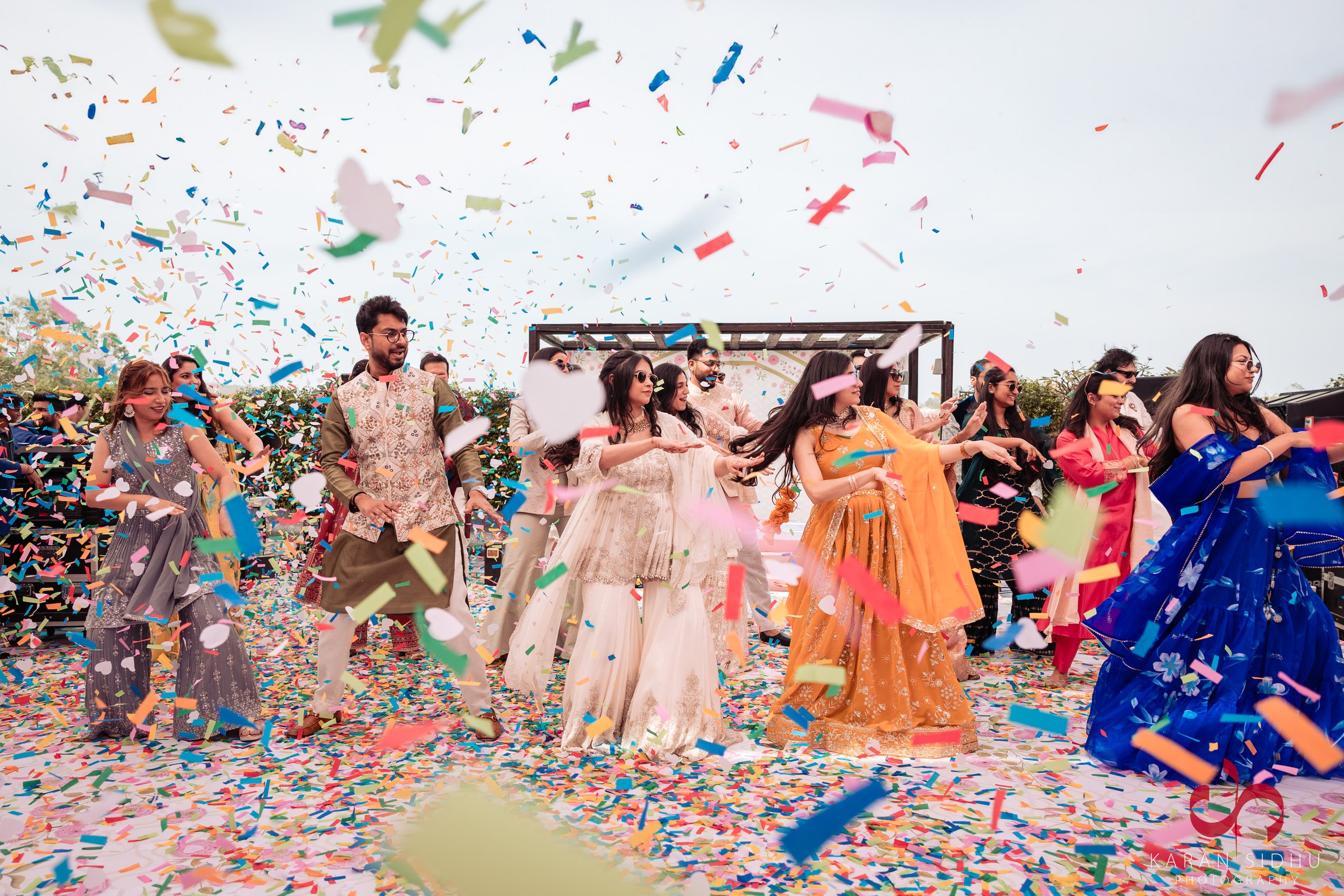Colorful celebration with people dancing amidst falling confetti and vibrant traditional Indian attire.