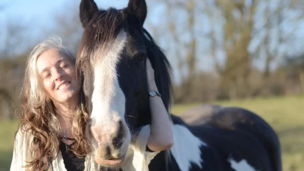 Liz with a horse in a field, and she is holding its head against hers