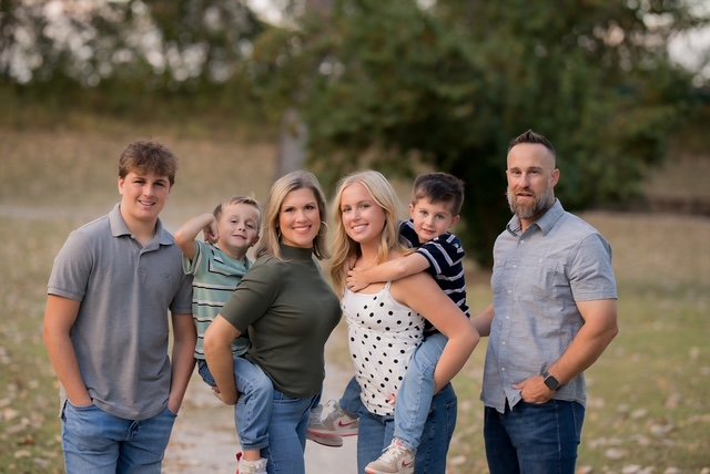 A family of six outdoors on a grassy field during daytime, smiling and posing for the photo.