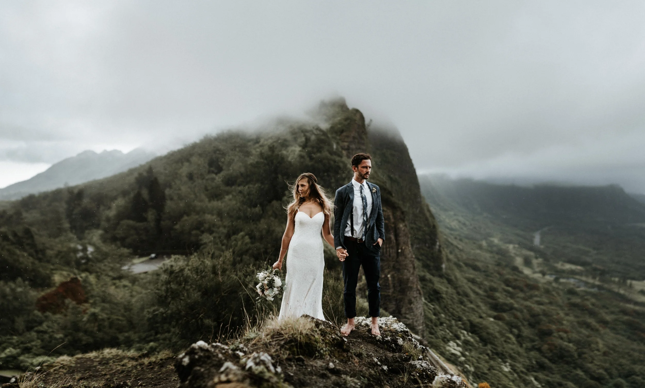 Bride and groom embracing on a lush cliff edge with misty mountains in the background, captured by Bend, Oregon wedding photographer Tony Gambino.