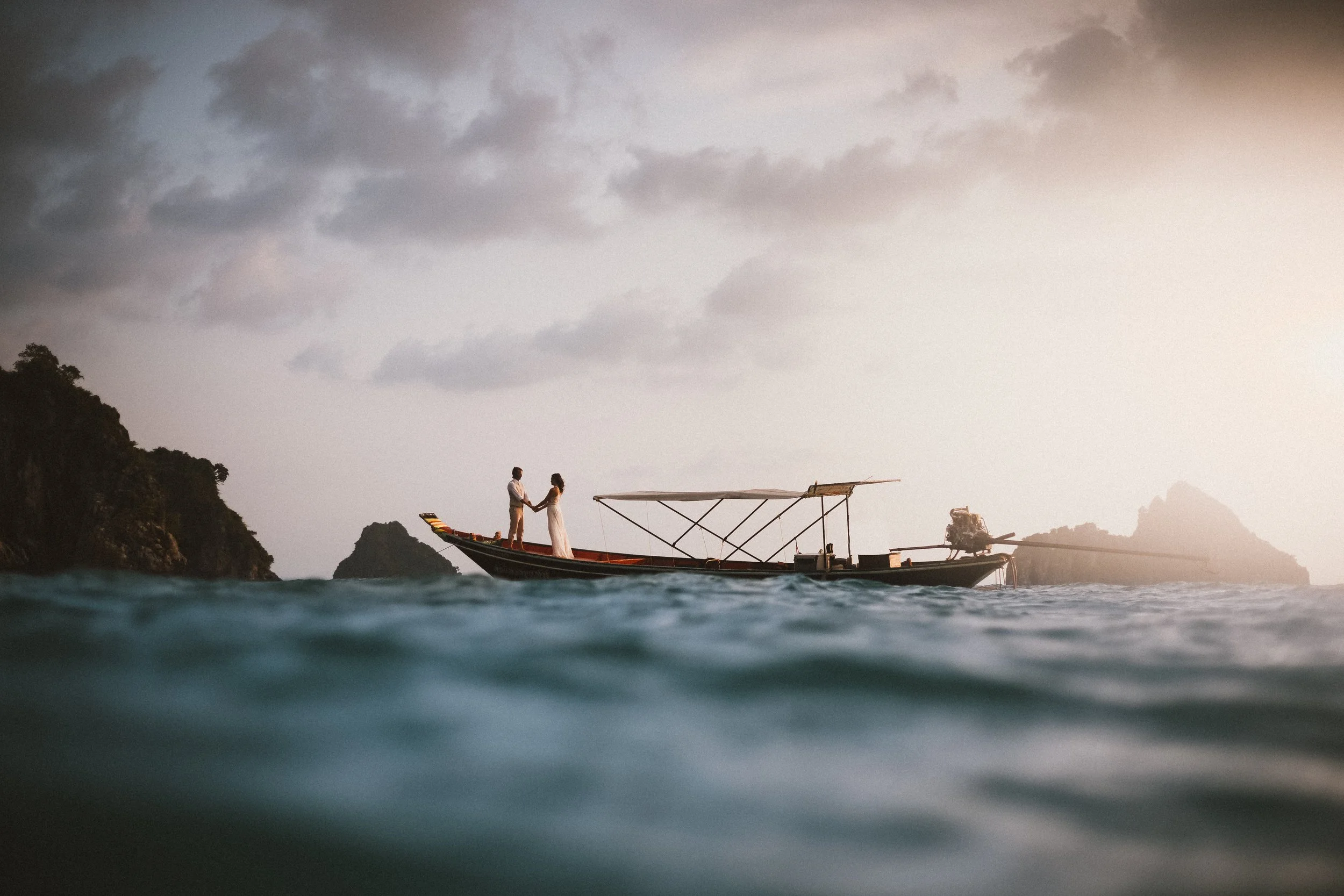 Newlywed couple seated in a small boat gliding across tranquil waters at sunset with distant mountains on the horizon, photographed by Bend, Oregon wedding photographer Tony Gambino.