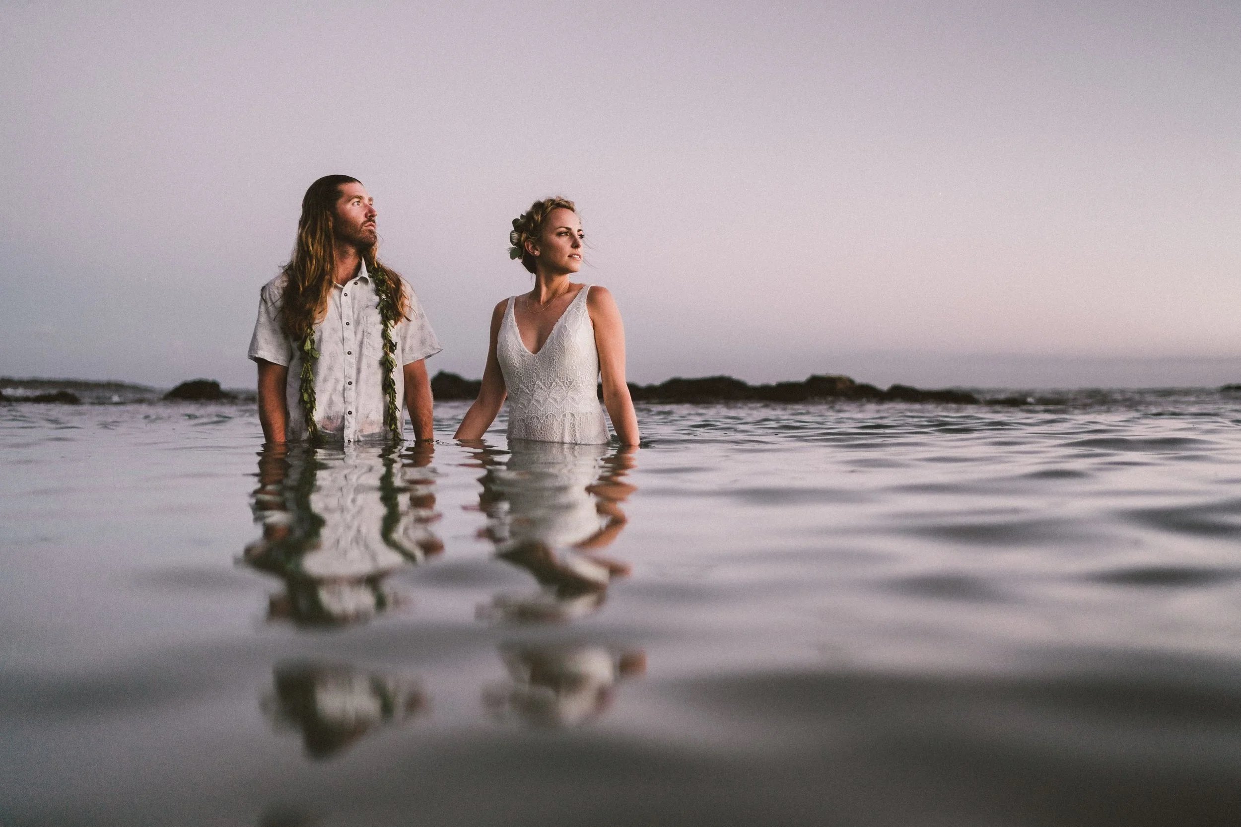 Bride and groom holding hands while standing knee‑deep in calm water at sunset, captured by Bend, Oregon elopement photographer Tony Gambino.