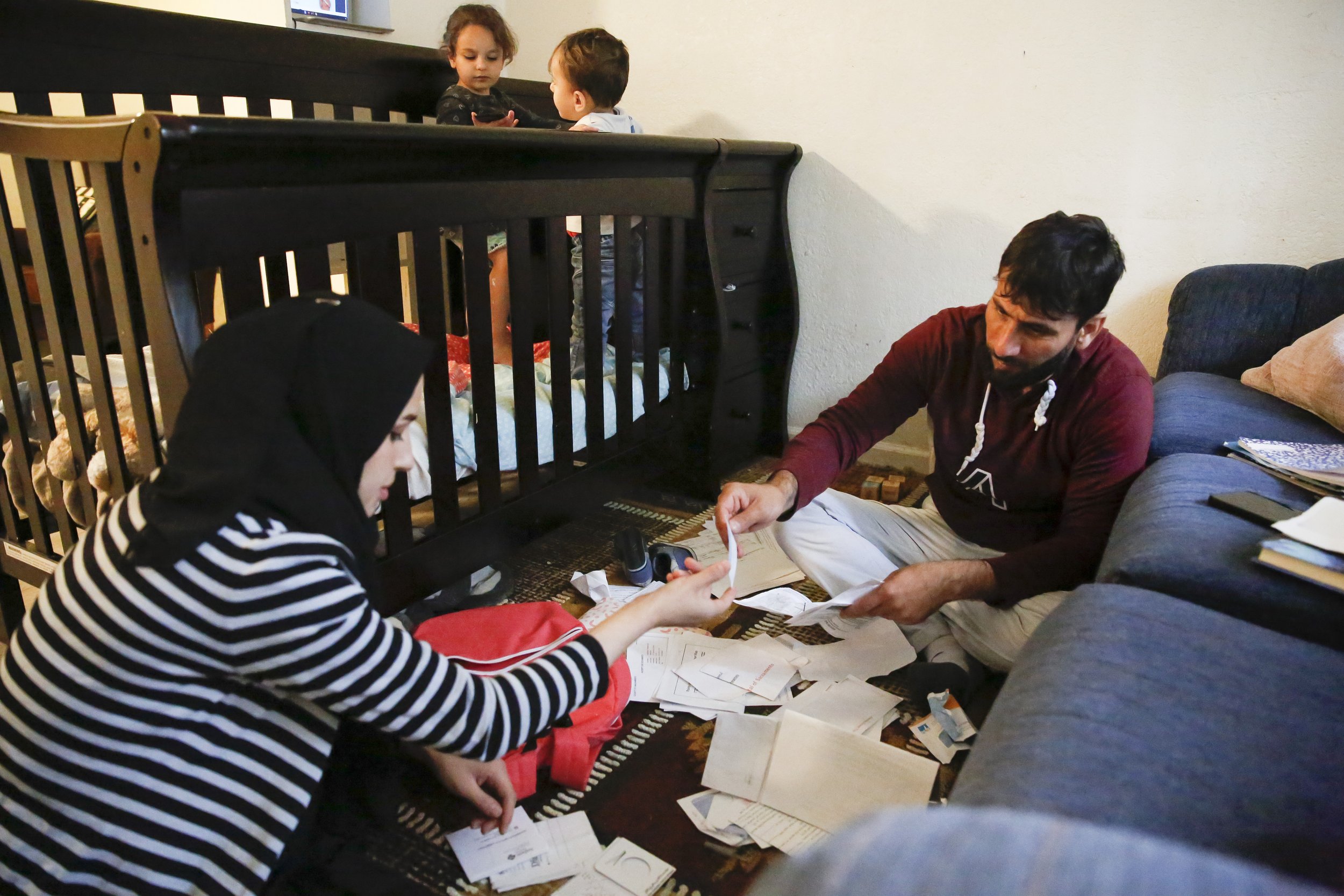  Najibullah Mohammadi and his wife Susan Mohammadi go through documents and bills on the floor of their living room while their children, Zahra and Yasar, play in the crib next to them on Thursday, April 14, 2022. Najibullah Mohammadi, his wife Susan