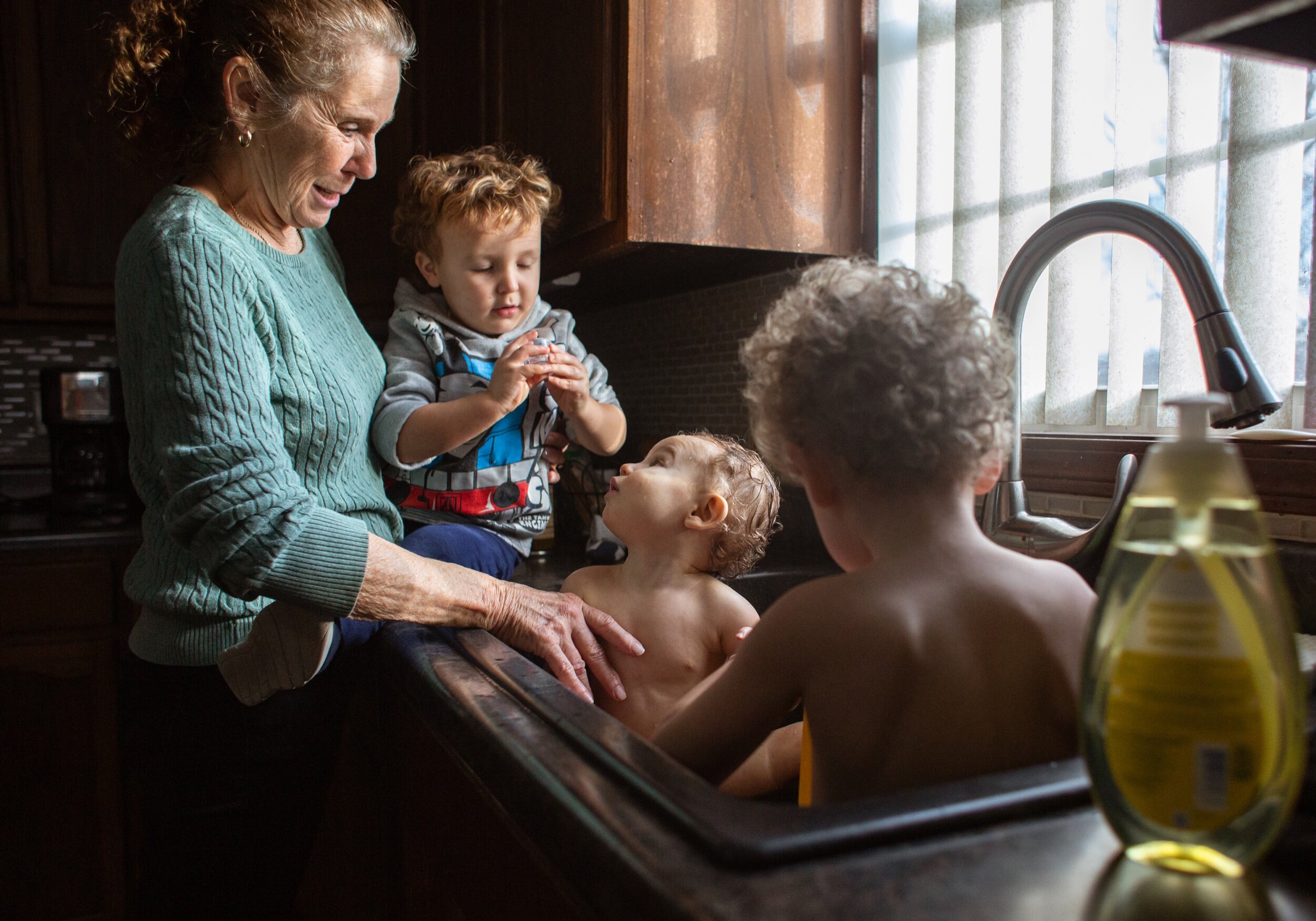Diane Blume watches her grandsons, Asher Stenftenagel, 1, center, and his brother Alec, 3, take a bath in her kitchen sink as their cousin, Benson Wahl, 2, all of Huntingburg, plays with a lid from a bottle of baby lotion at her home in Kyana on Fri