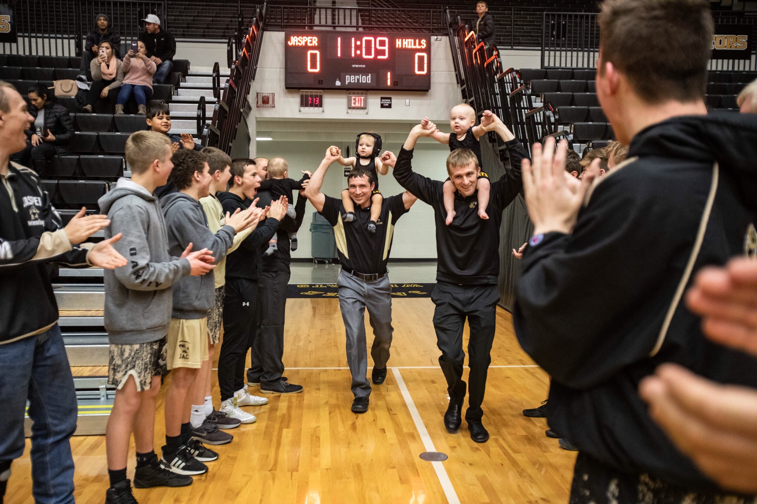 Jasper wrestling head coach Jace Brescher and his brother, varsity assistant coach Sean Brescher, hold their sons, Decker Brescher, 1, left, and Silas Brescher, 1, over their shoulders as they enter the gym for Thursday's boys wrestling match in Jas