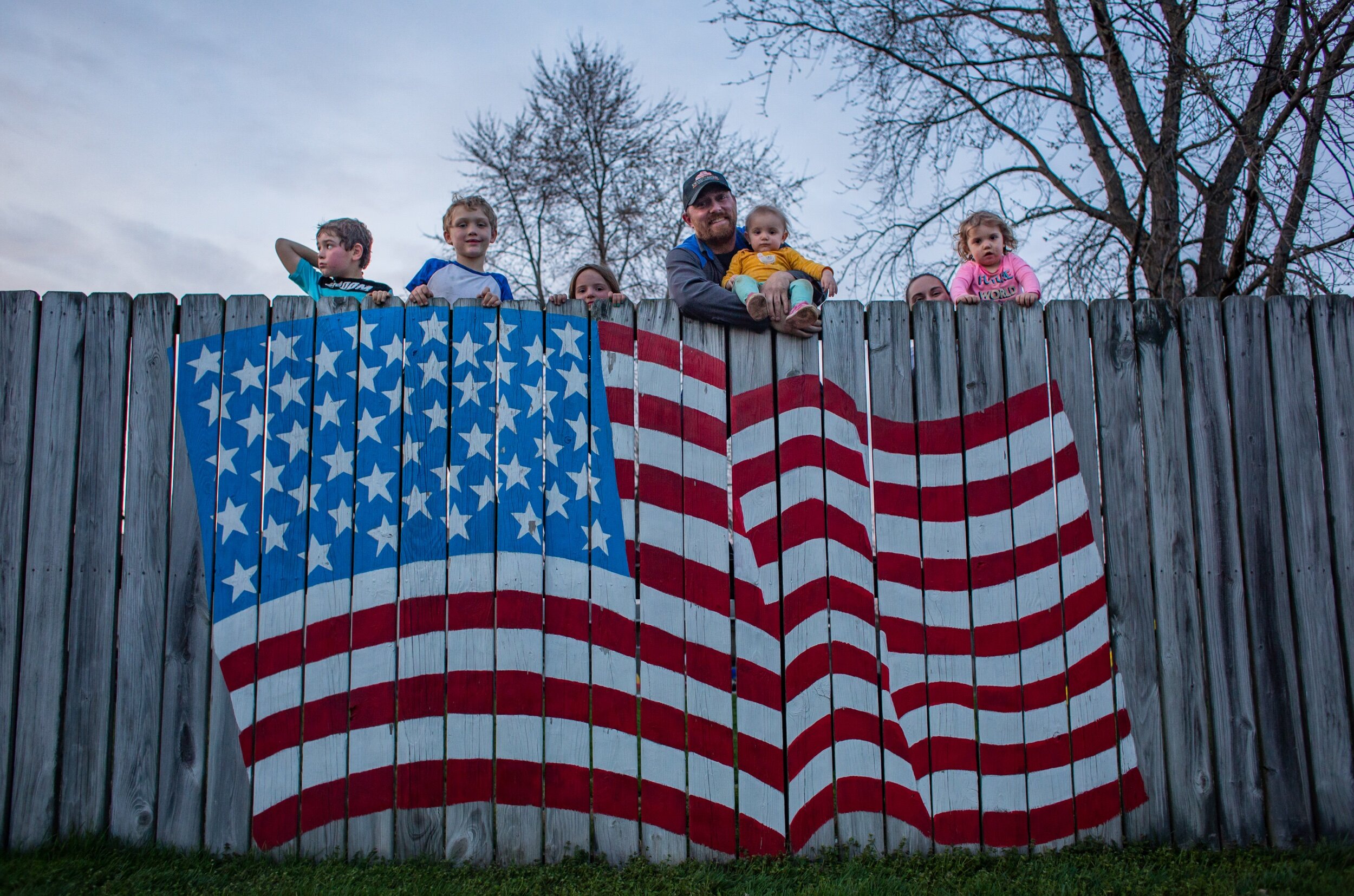The Ellis family of Holland, Rayland, 6, Torrin, 8, Reagan, 4, Joseph, Everlee, 1, Jennifer and Tinsley, 2, pose for a portrait over their fence on March, 26, 2020. Jennifer had the American flag mural painted for her husband, Joseph, during his 201