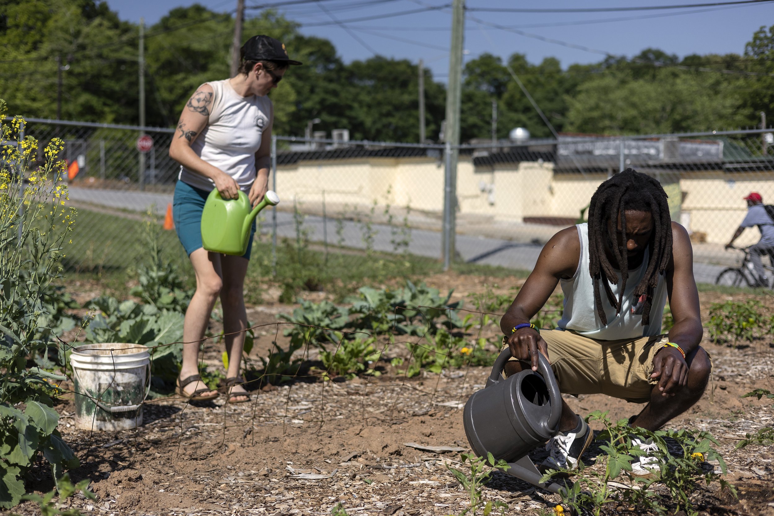  Broderick Flanigan, local artist and community activist, right, waters vegetables in Farm to Neighborhood’s community garden on Thursday, June 2, 2022 in Athens. The garden was established in 2018 and serves residents primarily in the Nellie B neigh