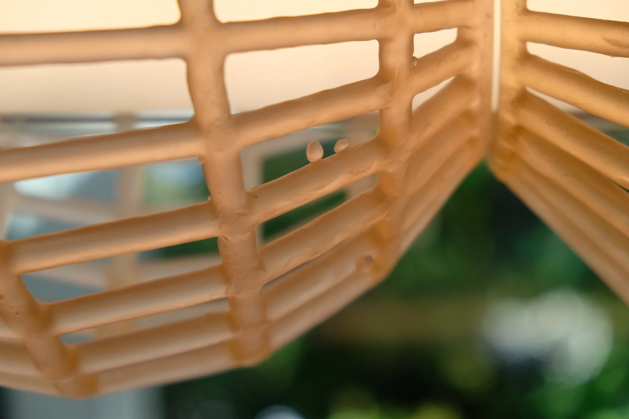 Close-up of a beige lattice structure, possibly made of wood or wicker, with a blurred green background.